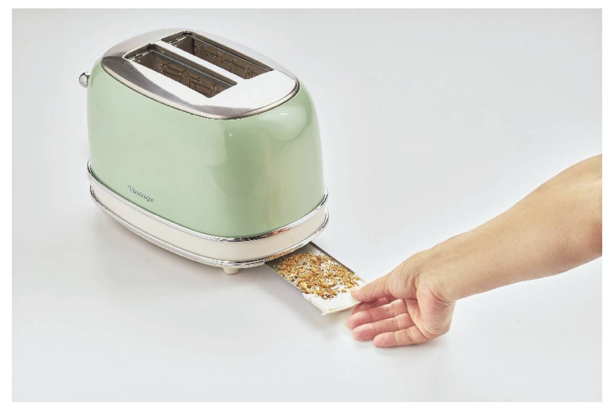 Eine Hand legt eine Scheibe Brot mit Samen in einen grünen Zweischlitz-Toaster.