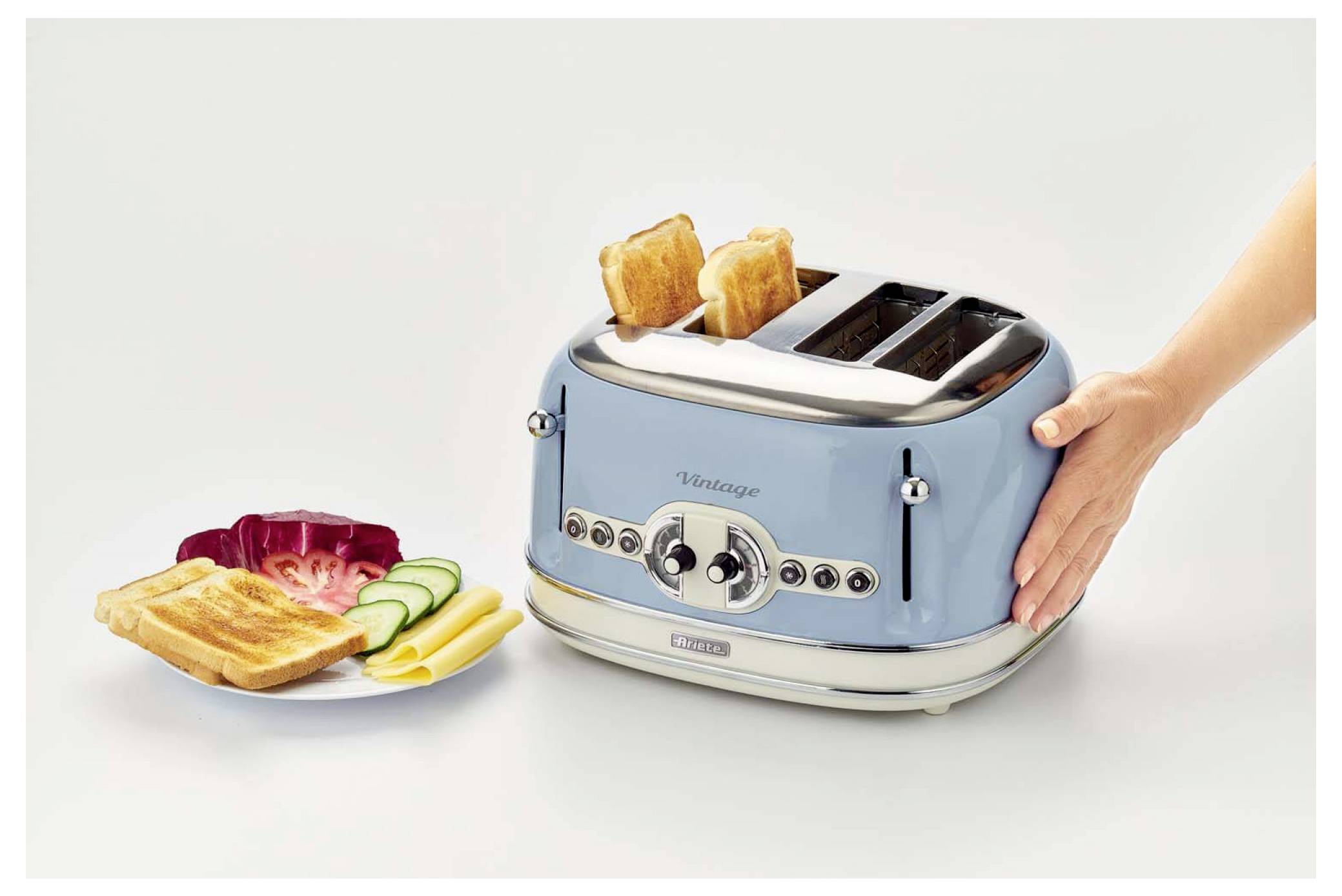 Blauer Vier-Schlitz-Toaster mit zwei Scheiben, die neben einem Teller mit getoastetem Brot und geschnittener Gurke hochspringen, zeigt eine Frühstücksgarnitur.