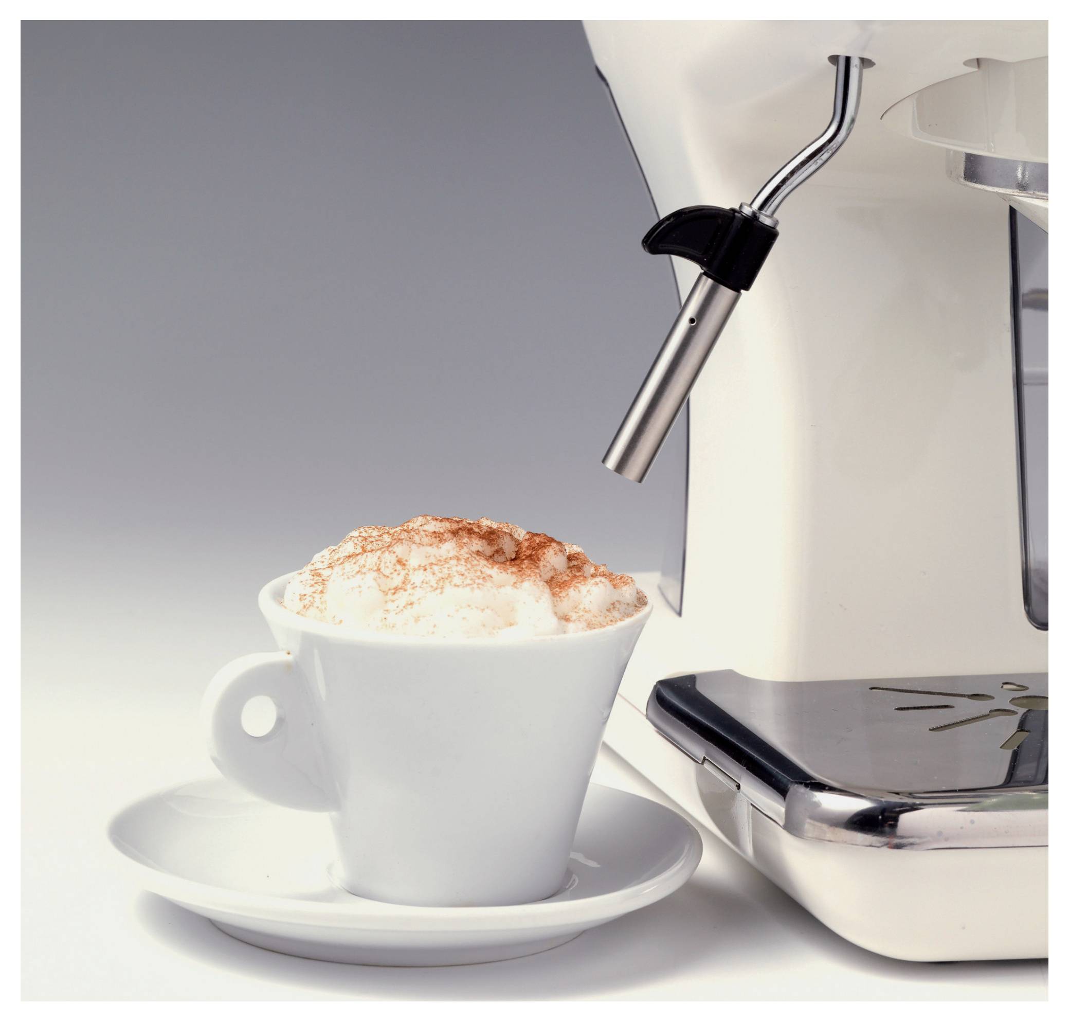 Weiße Tasse mit schäumigem Kaffee auf einer Untertasse neben einer Edelstahl-Espressomaschine, die Schaum abgibt