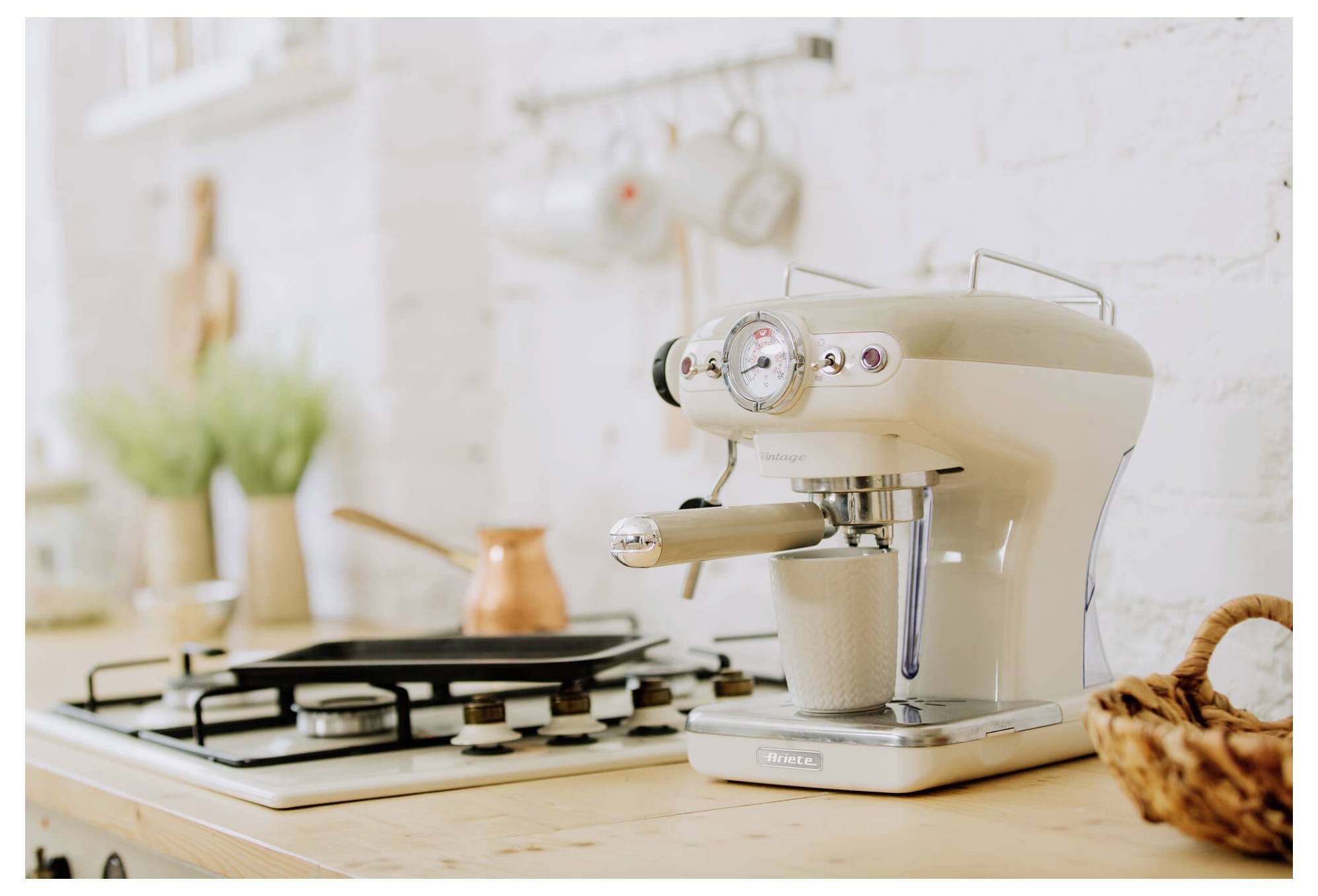 Cremefarbene Espressomaschine, die eine Tasse auf einer Küchenarbeitsplatte neben einem Gasherd und einem Kupfertopf braut.