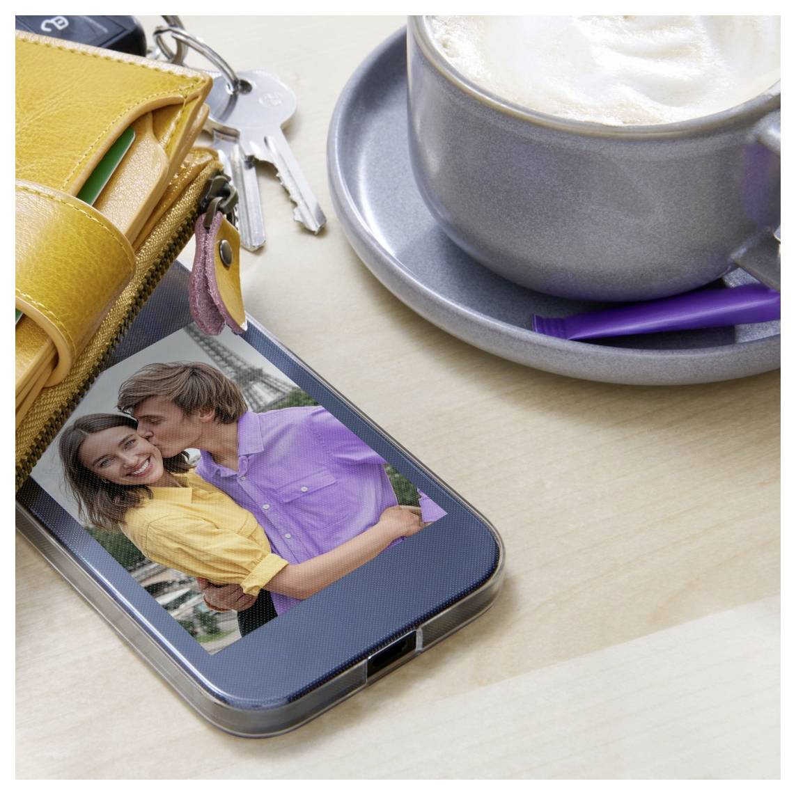 Smartphone auf einem Schreibtisch zeigt ein umarmendes Paar auf dem Bildschirm neben einer Kaffeetasse, Schlüsseln und einem gelben Geldbeutel.