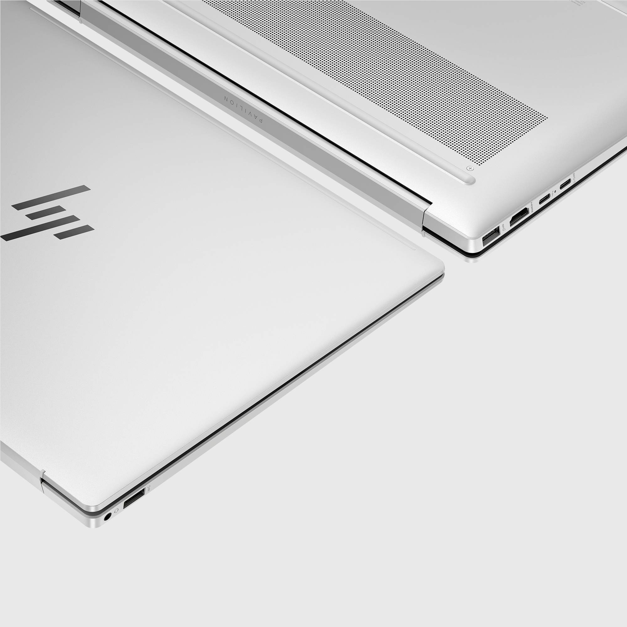 Zwei schlanke silberfarbene Laptops überlappen sich auf weißem Hintergrund und zeigen ihre geschlossenen Deckel, Lüftungsschlitze und seitliche Anschlüsse.