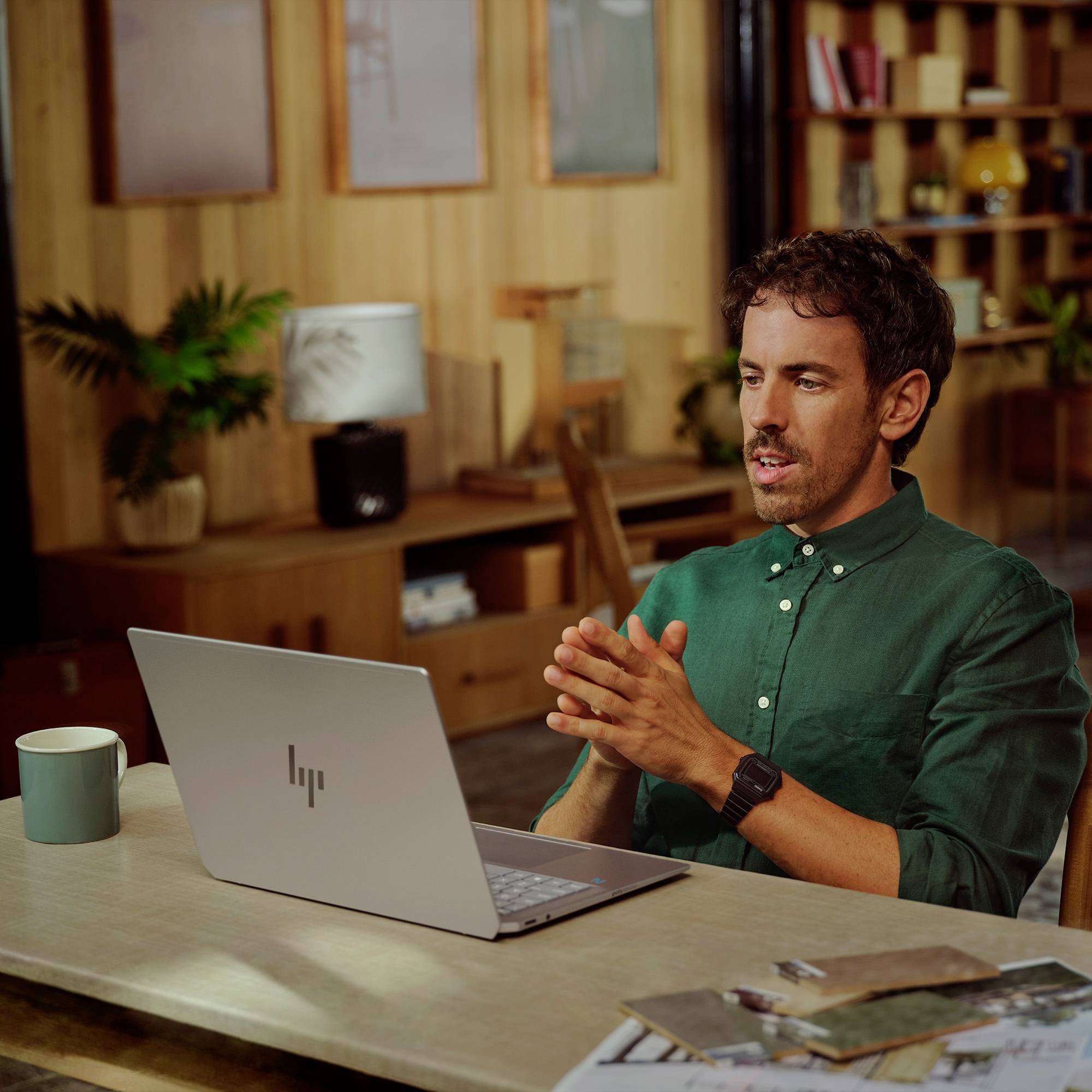Ein Mann spricht in einem Videoanruf aus einem Heimzimmer, sitzt an einem Schreibtisch mit einem Laptop und einer Kaffeetasse, die Hände verschränkt während er spricht.