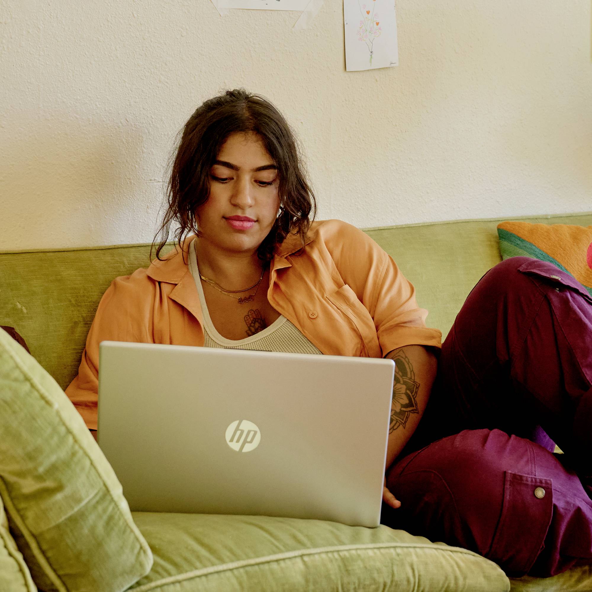 Frau sitzt auf einem Sofa und benutzt einen HP-Laptop, sie wirkt konzentriert, während sie zu Hause arbeitet oder lernt.