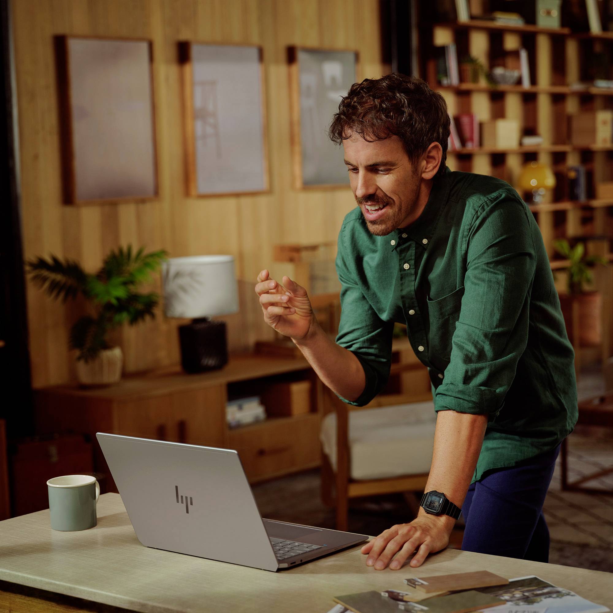 Ein Mann, der während eines Videoanrufs auf einem Laptop lächelt und spricht, lehnt sich über einen Schreibtisch in einem gemütlichen Homeoffice.