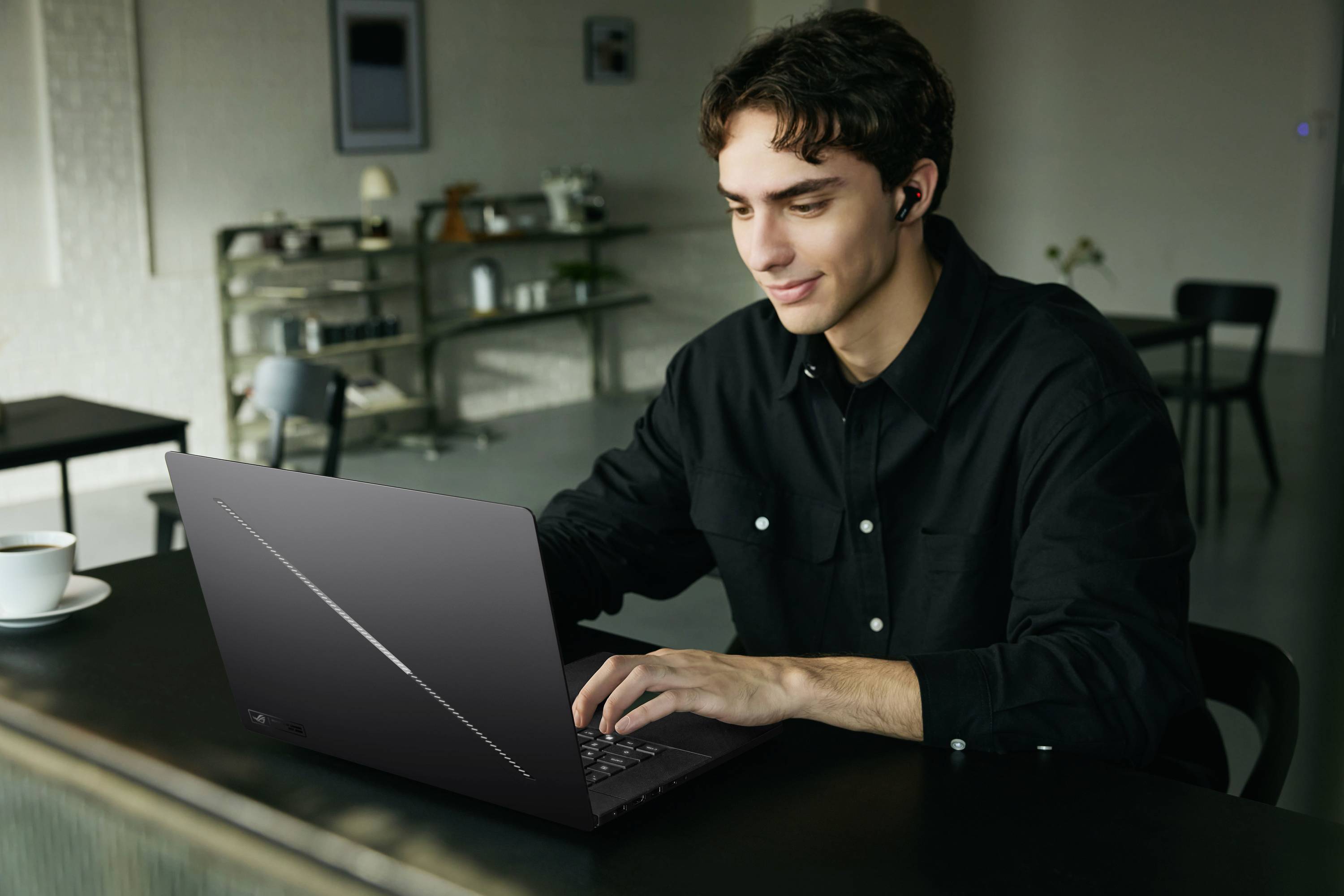 Junger Mann mit Kopfhörern arbeitet an einem Laptop an einem Cafétisch und konzentriert sich auf das Tippen, während eine Kaffeetasse in der Nähe steht.