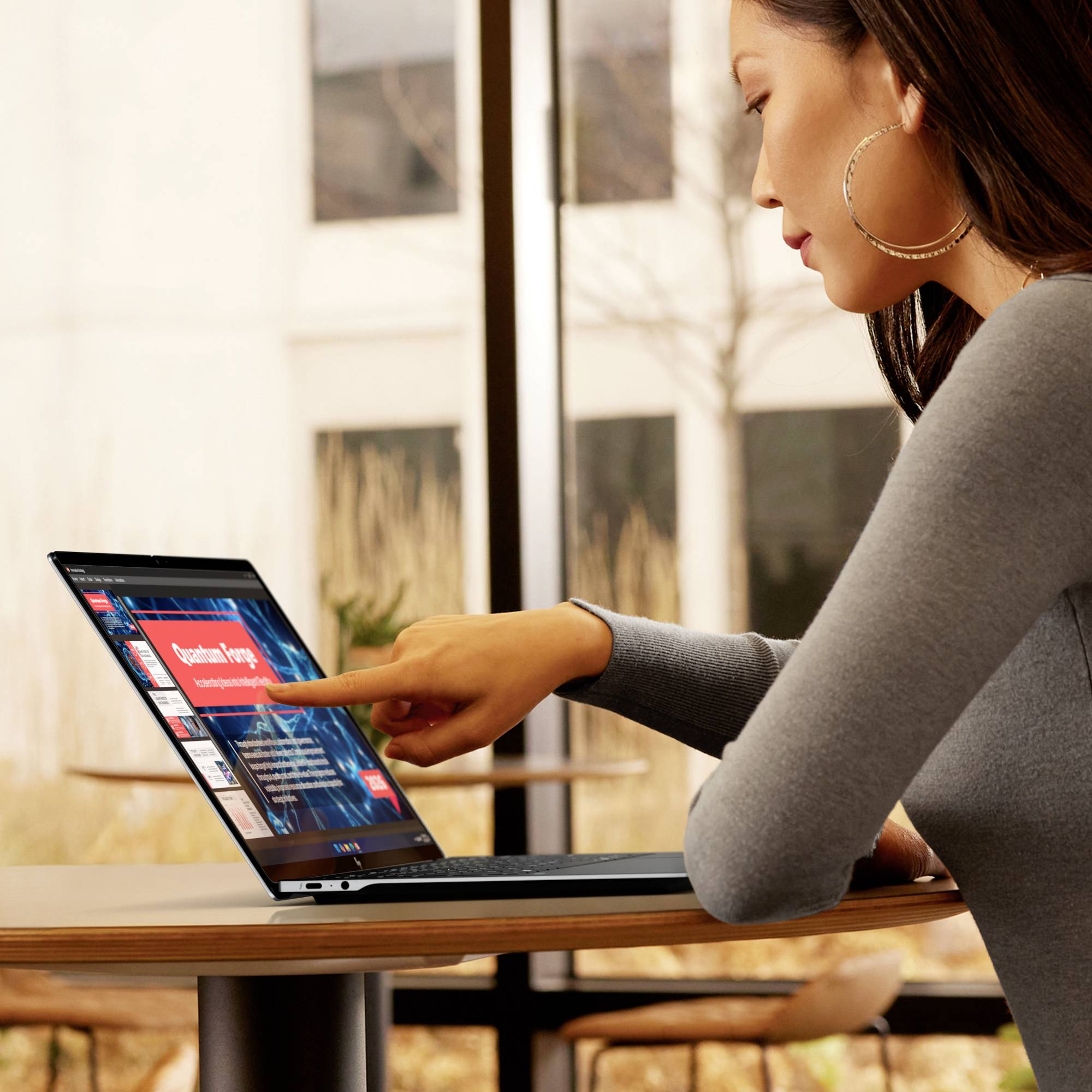 Frau, die an einem Tisch einen Laptop benutzt und auf eine Webseite auf dem Bildschirm in einer hellen Innenumgebung zeigt.