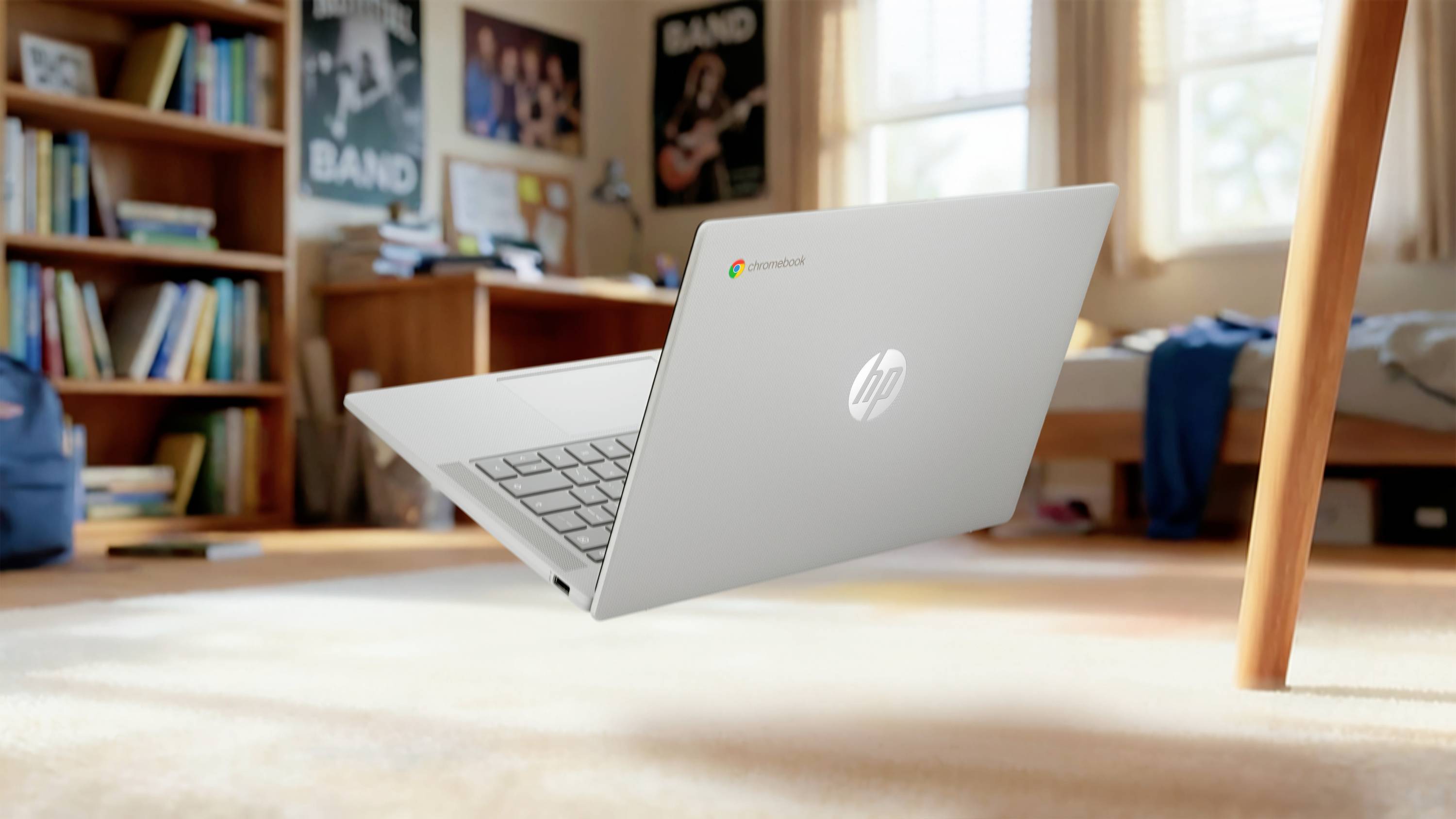 Ein schwebendes HP-Laptop über einem teppichbedeckten Schlafzimmer oder Wohnheim, mit einem Schreibtisch, Bett und Postern im Hintergrund.