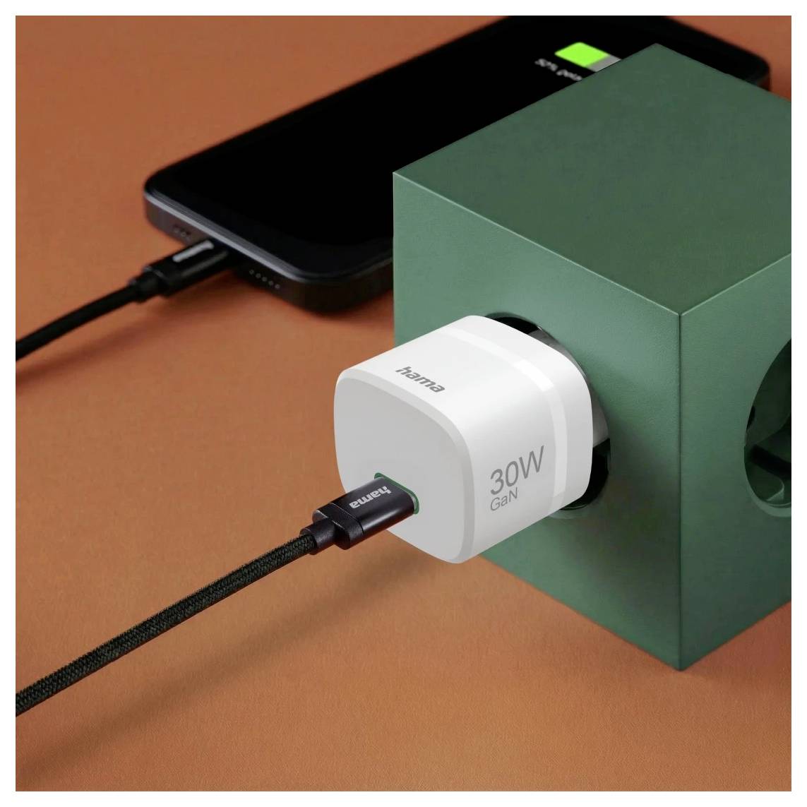 Weißes 30W-GaN-Ladegerät in einen grünen Würfel gesteckt, das ein Smartphone mit geflochtenen USB-C-Kabeln auf einer orangefarbenen Oberfläche lädt.