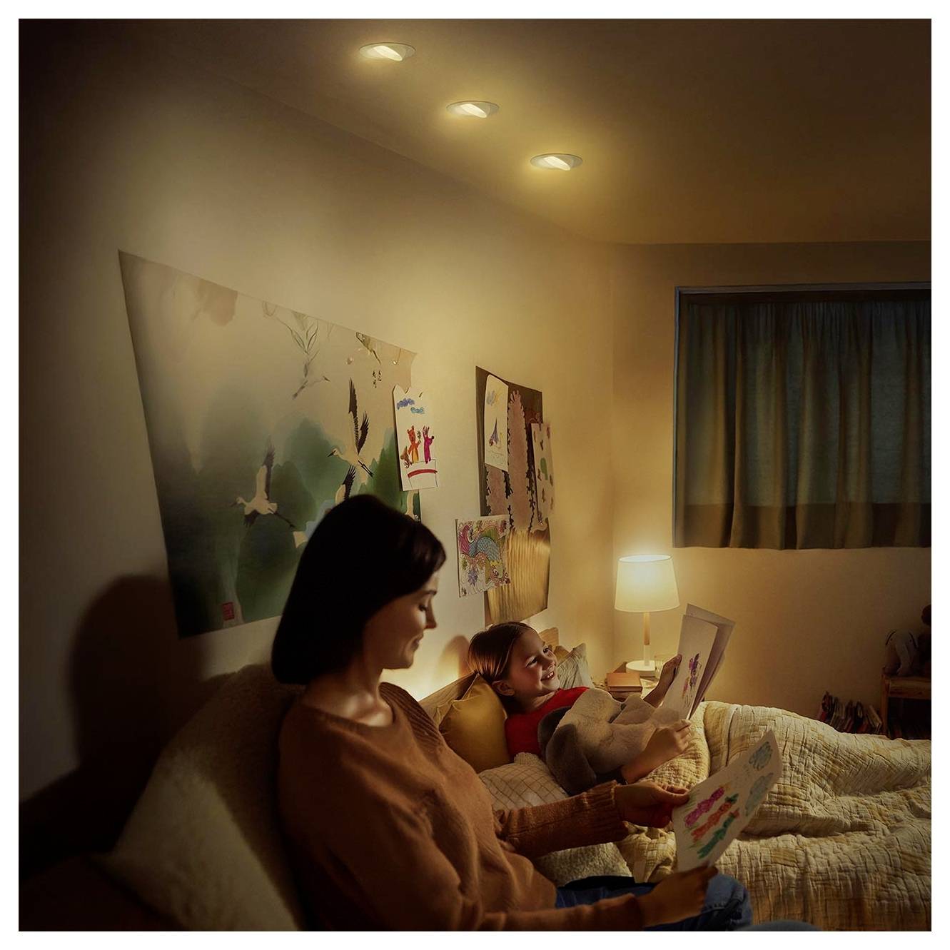 Frau und Kind sitzen in einem dunklen Schlafzimmer und lesen nachts zusammen Bücher bei Licht einer Nachttischlampe.