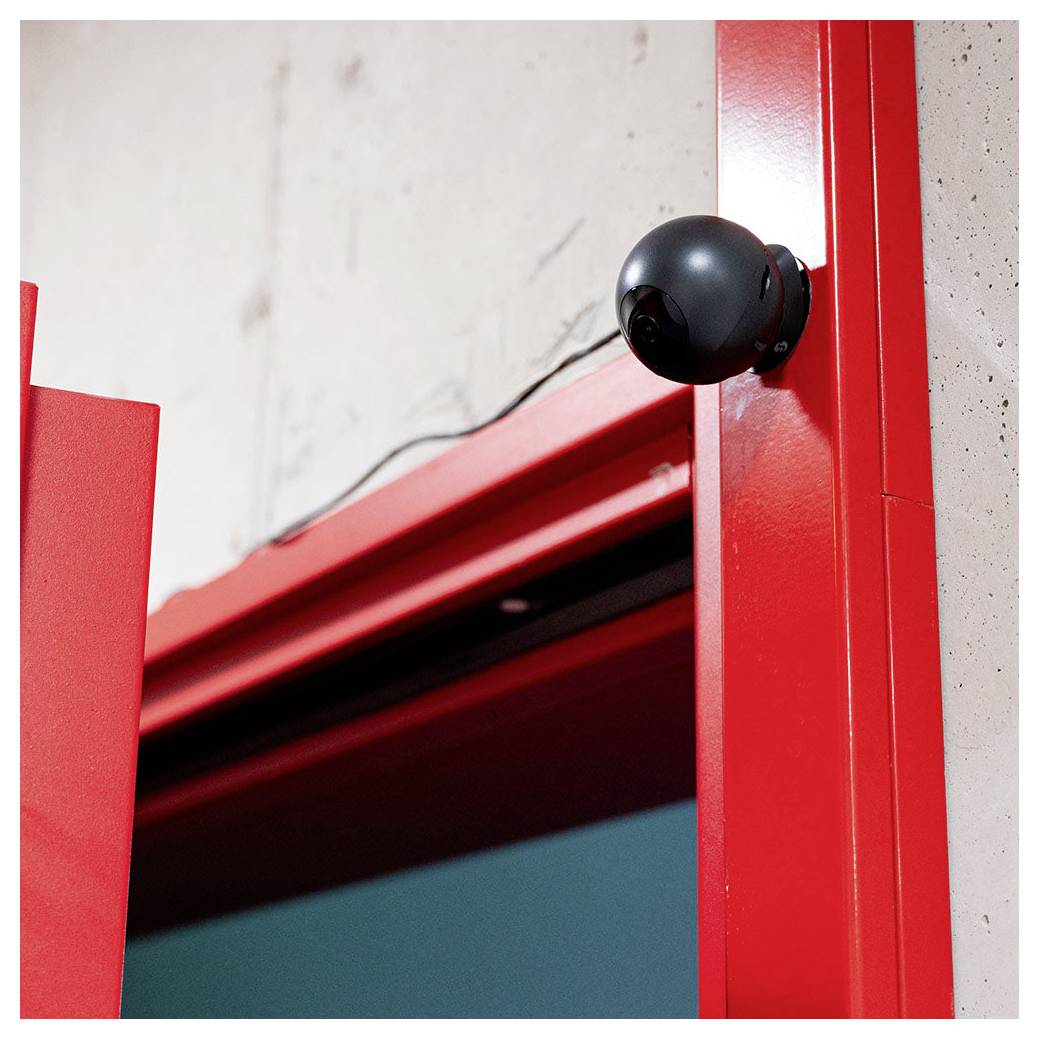Nahaufnahme einer leuchtend roten Türöffnung mit einem schwarzen kugelförmigen Türstopper oder Scharnierwerk gegen eine helle Wand.