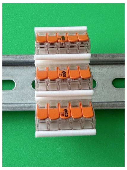 Drei elektrische Steckverbinder an einer Metallmontageschiene vor grünem Hintergrund befestigt.