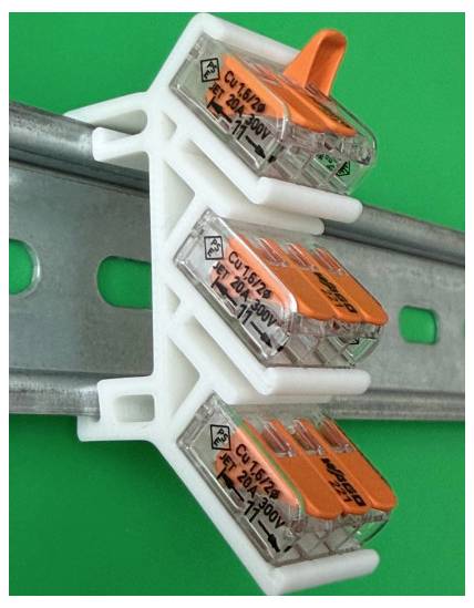 Drei elektrische Steckverbinder mit Clips auf einer Metallschiene, mit orangefarbenen Hebeln vor grünem Hintergrund.