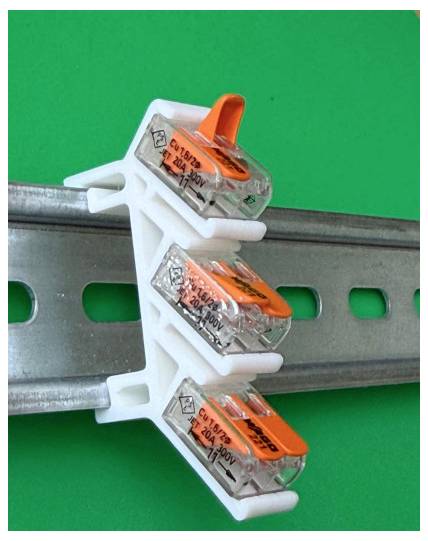 Drei elektrische Steckverbinder, die auf eine metallische DIN-Schiene vor grünem Hintergrund geklipst sind.