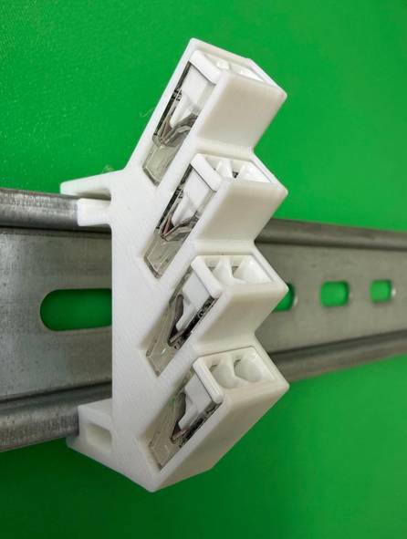 Weißer elektrischer Anschlussblock, der auf einer Metall-DIN-Schiene vor grünem Hintergrund aufgeclipst ist.
