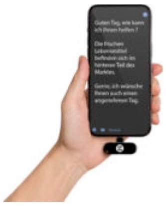 Eine Hand hält ein Smartphone im Dunkelmodus mit unscharfem deutschem Text, mit einem kleinen angebrachten Zubehörteil am unteren Ende des Telefons.
