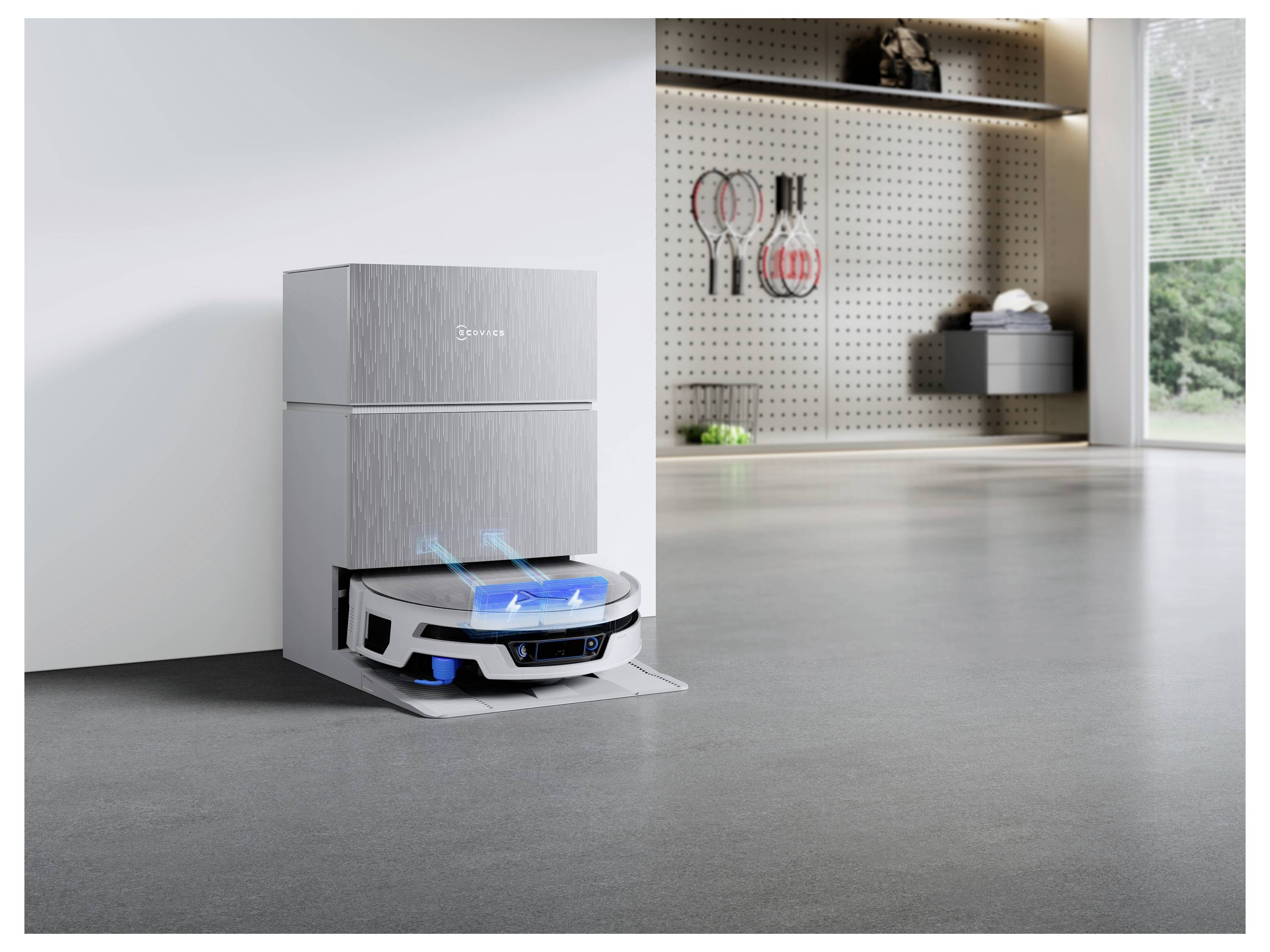 Ein Roboterstaubsauger dockt an und lädt neben einem Schrank in einem modernen Zimmer auf, mit Reinigungswerkzeugen und einem hellen Fenster im Hintergrund.