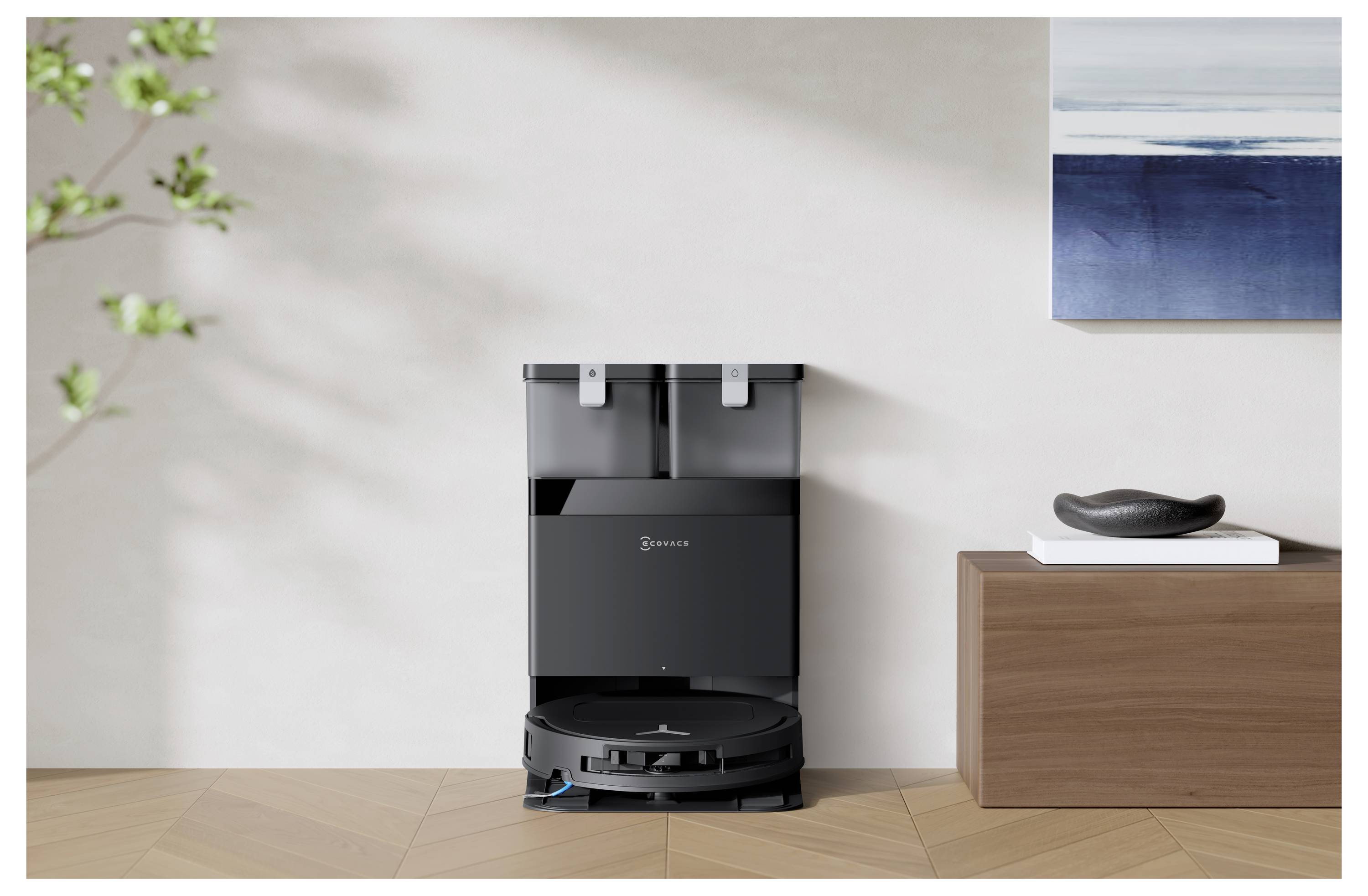 Schwarzer Roboterstaubsauger an der Wand angedockt in einem minimalistischen Raum, neben einem Holzschrank und Wandkunst.