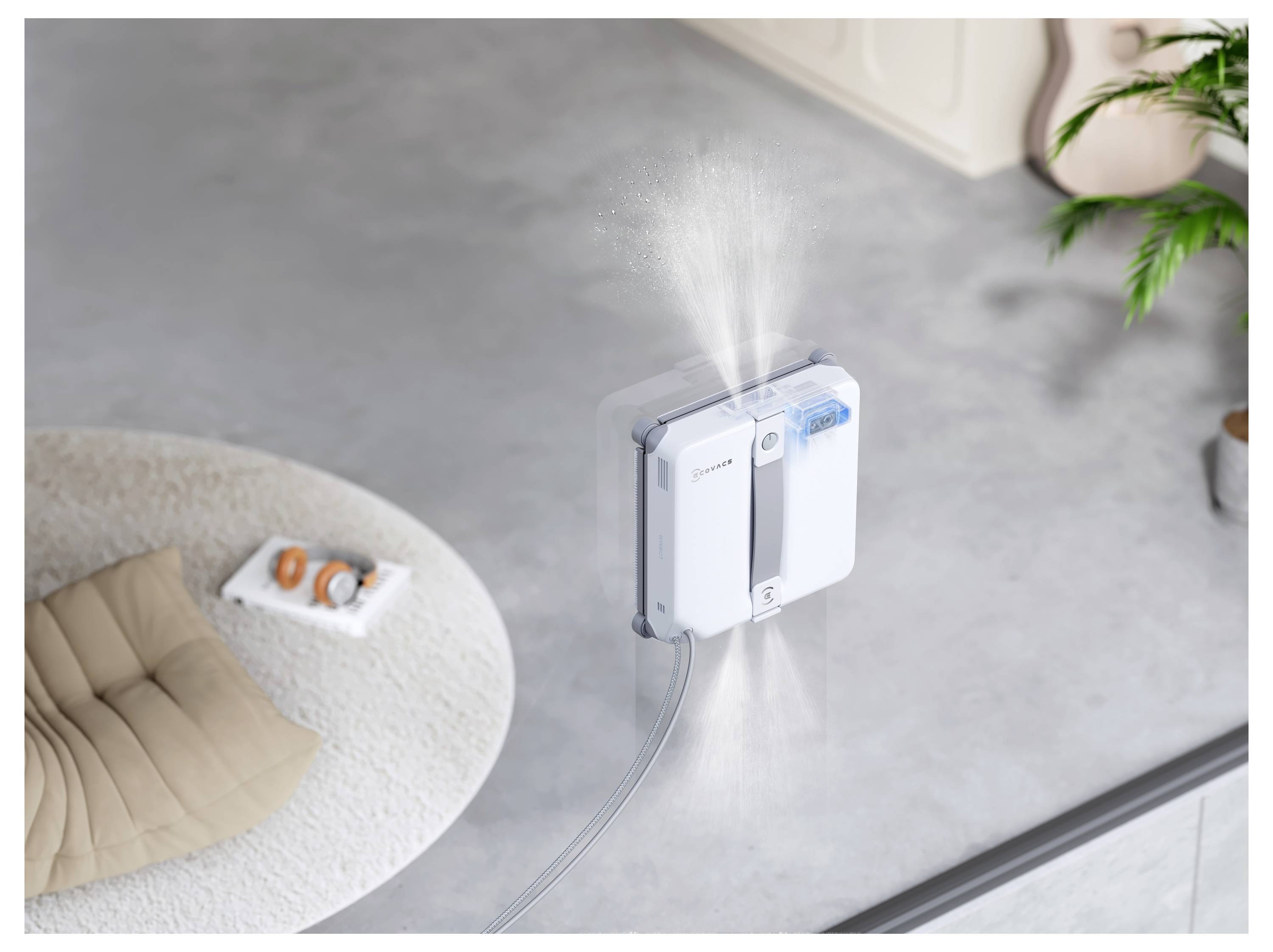 Ein Fensterputzroboter ist an einer Glasscheibe befestigt und sprüht Nebel beim Reinigen, von oben in einem modernen Raum betrachtet.