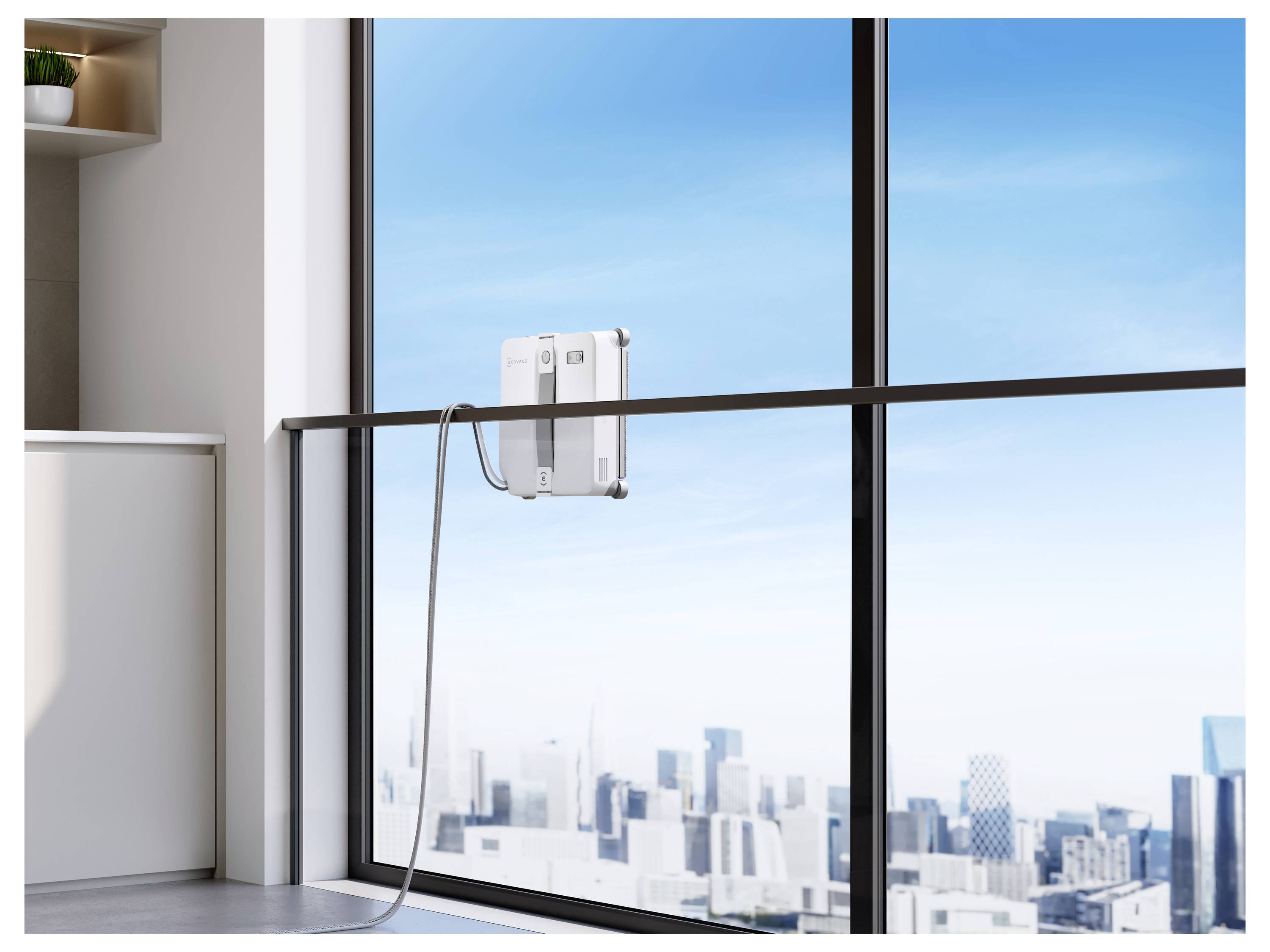 Ein Fensterreinigungsroboter, der auf einem raumhohen Glasfenster montiert ist, mit einem Stromkabel, das über einer Stadtsilhouette nach unten hängt.
