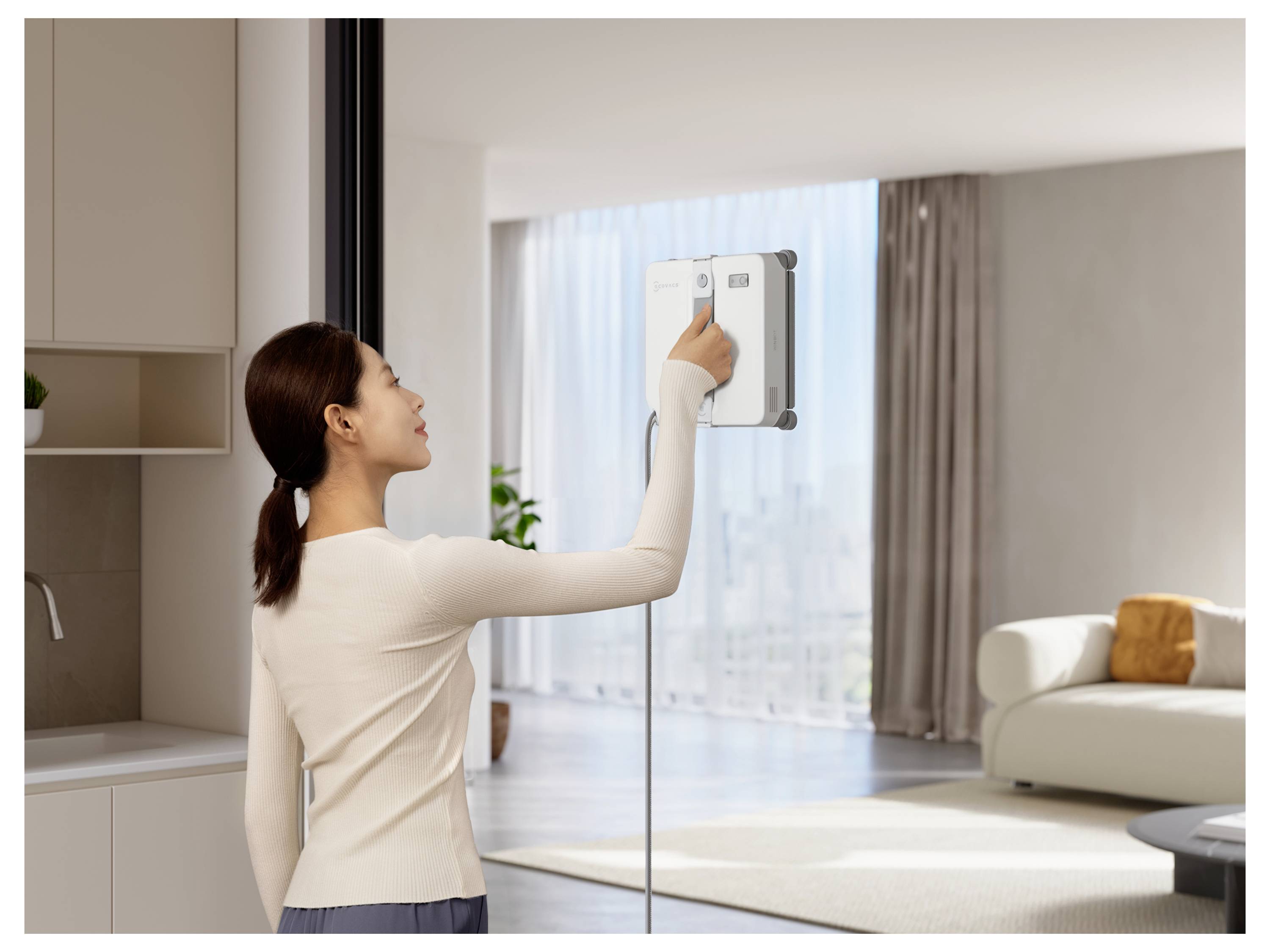 Frau stellt einen wandmontierten Thermostat in einem hellen, modernen Wohnzimmer ein.