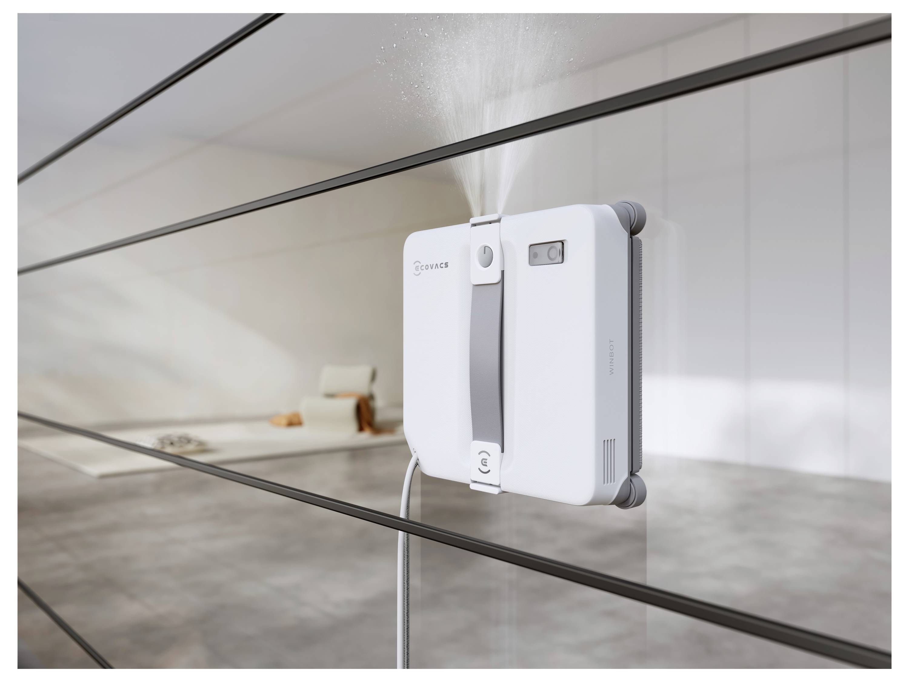 Ein weißes robotisches Fensterreinigungsgerät ist an einer Glasscheibe befestigt und sprüht Wasser, während es das Fenster reinigt.
