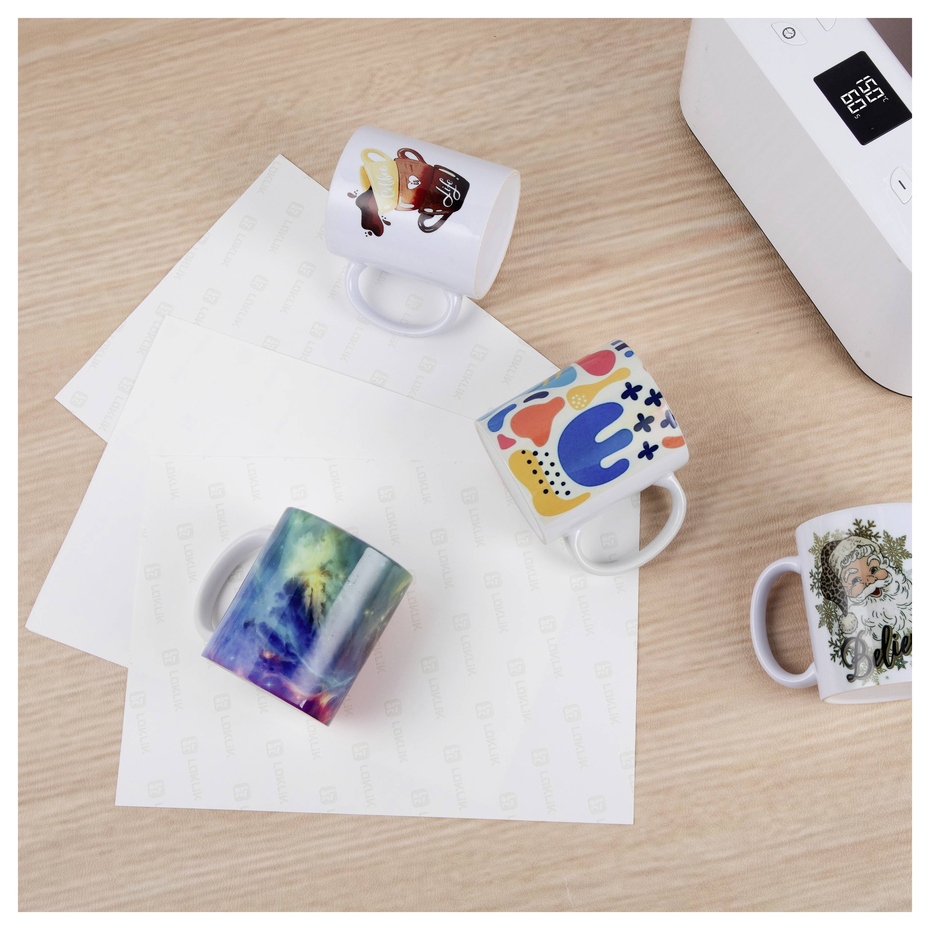 Mehrere benutzerdefinierteMugs auf Transferfolien neben einer Mugpresse auf einem Holztisch.