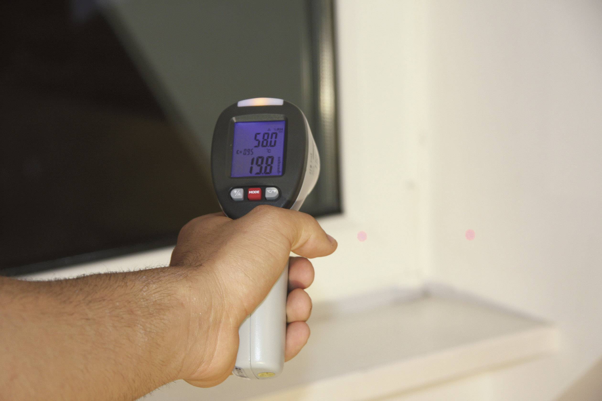 Eine Hand hält ein Infrarotthermometer, das auf eine Oberfläche gerichtet ist. Display zeigt '58,0°C' an.