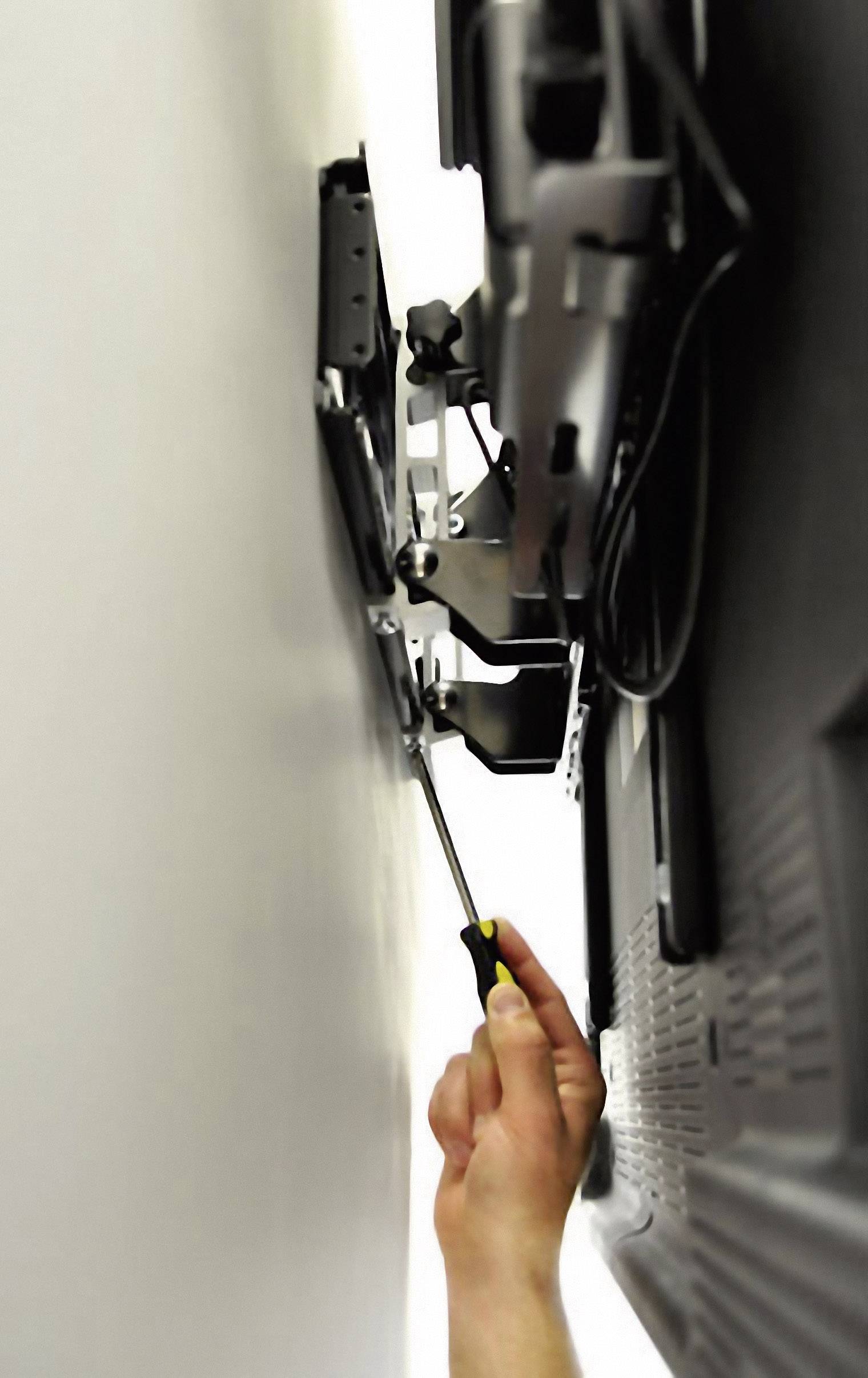 Eine Hand zieht mit einem Schraubendreher eine Schraube an, um einen Fernseher an einer Wandhalterung zu befestigen.