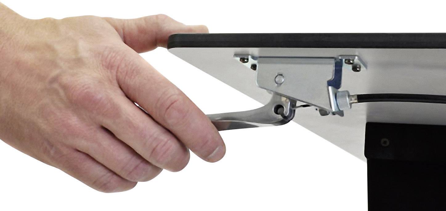 Hand betätigt einen Hebel unter einer Tischkante, Verbindung zu einer Metallhalterung sichtbar.