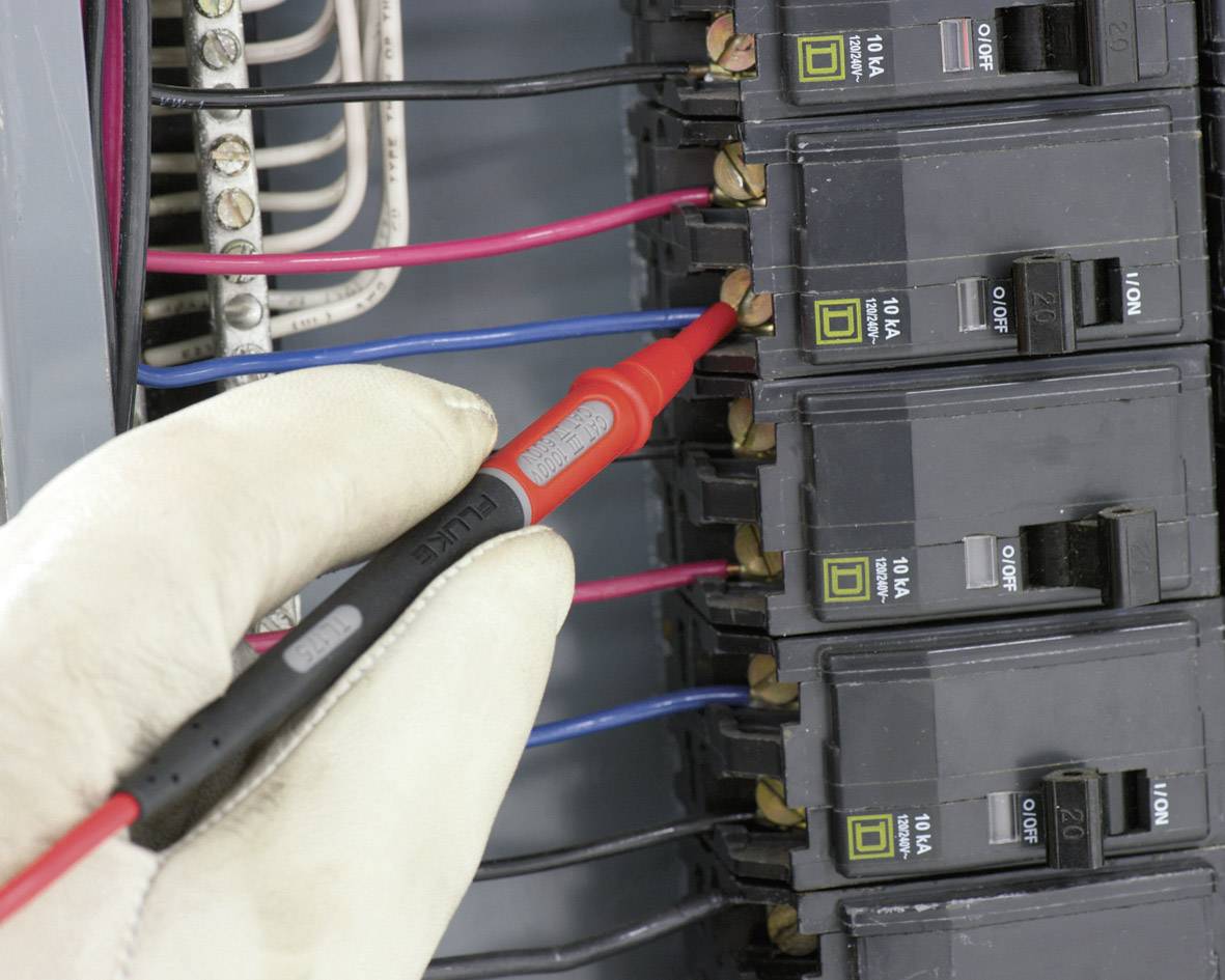 Eine Hand mit Handschuh hält einen Prüfgerätstift an einem Sicherungsschalter in einem elektrischen Sicherungskasten für Spannungsprüfung.