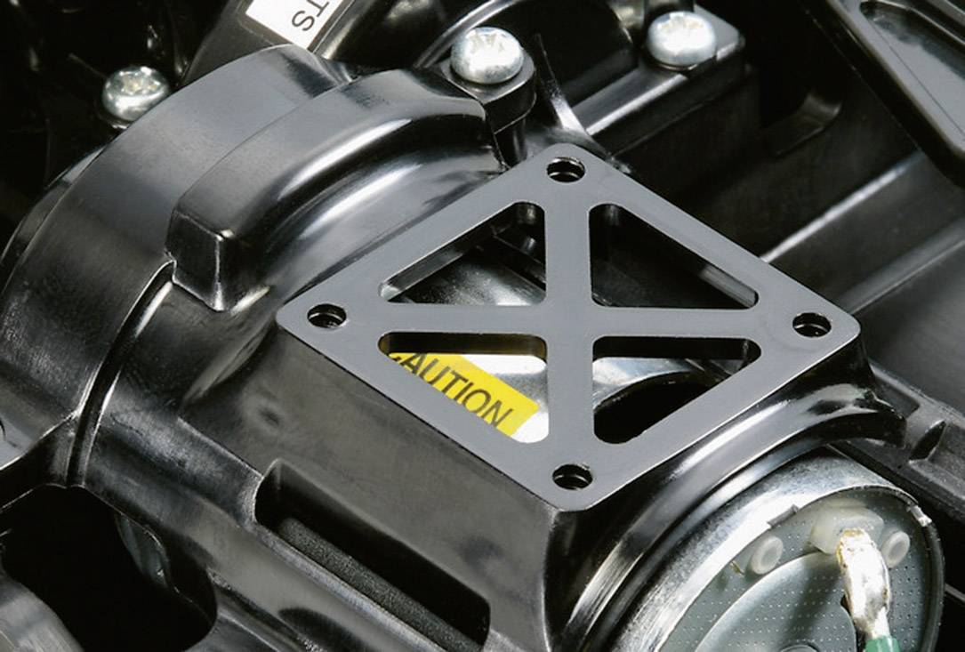 Maschinenteil mit schwarzer Metallhalterung. Ein Gelb-weißes Warnschild ist teilweise sichtbar.