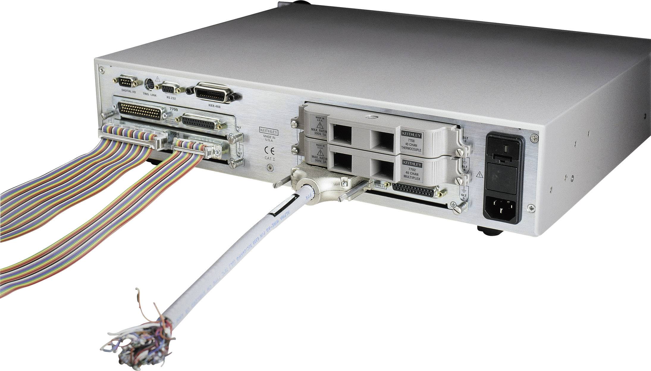 Rückseite eines elektronischen Geräts mit mehreren Anschlüssen und Kabeln. Links verläuft ein mehradriges Flachbandkabel.