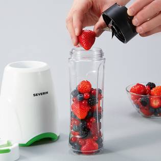Person steckt Erdbeere in kleinen Mixer, der mit Beeren gefüllt ist. Rechts eine Schüssel mit Beeren, links Mixerbasis.