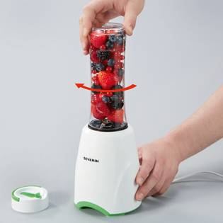 Person füllt einen Mixer mit Beeren. Der Mixer ist weiß mit grünem Akzent. Eine Hand hält den Deckel. Der Mixvorgang wird demonstriert.