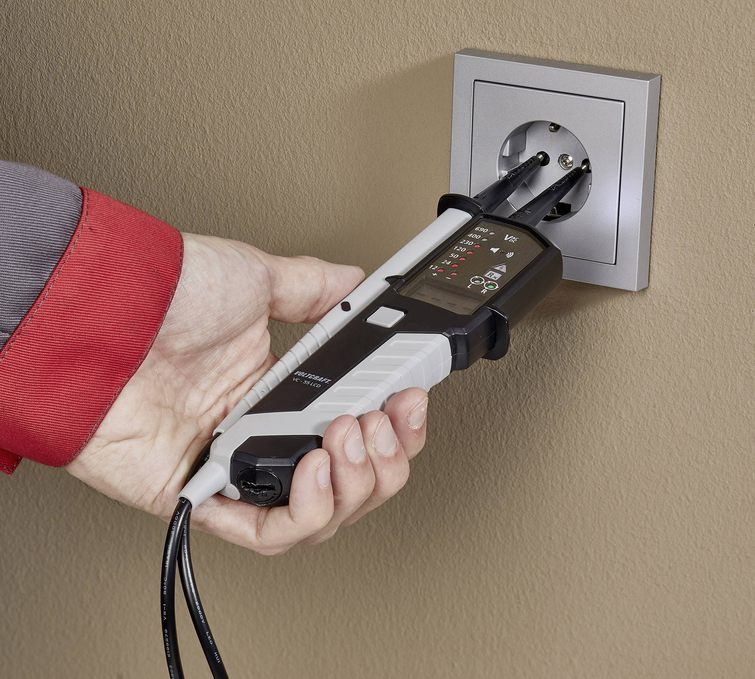 Eine Hand hält ein Spannungsprüfgerät, das in eine Wandsteckdose gesteckt ist, um elektrische Spannung zu testen.