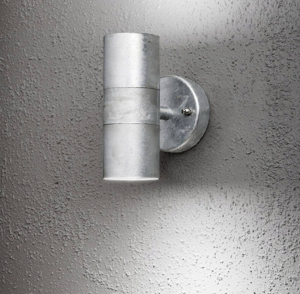 Eine silberne Wandleuchte mit zylindrischem Design an einer grauen, strukturierten Wand.