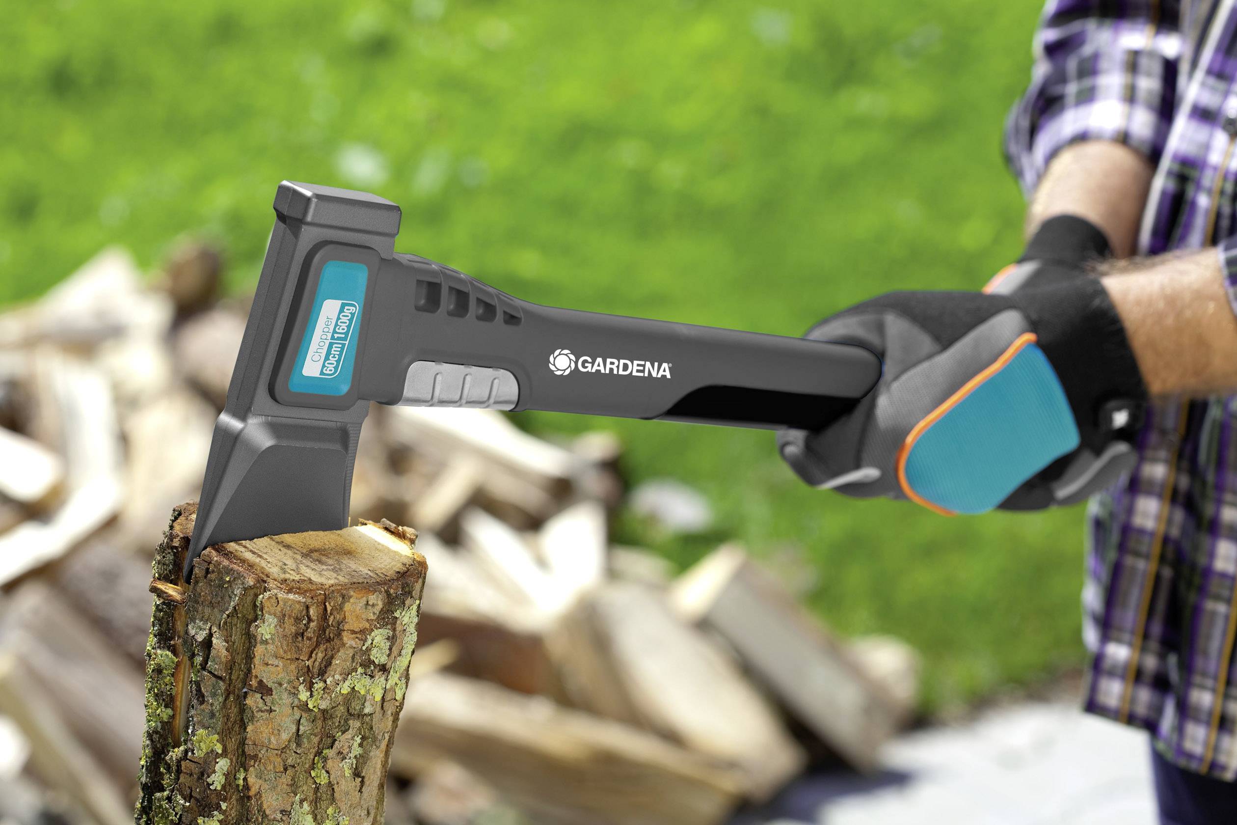 Eine Person mit Handschuhen hackt Holz mit einer Axt. Im Hintergrund ist ein grüner Rasen zu sehen.