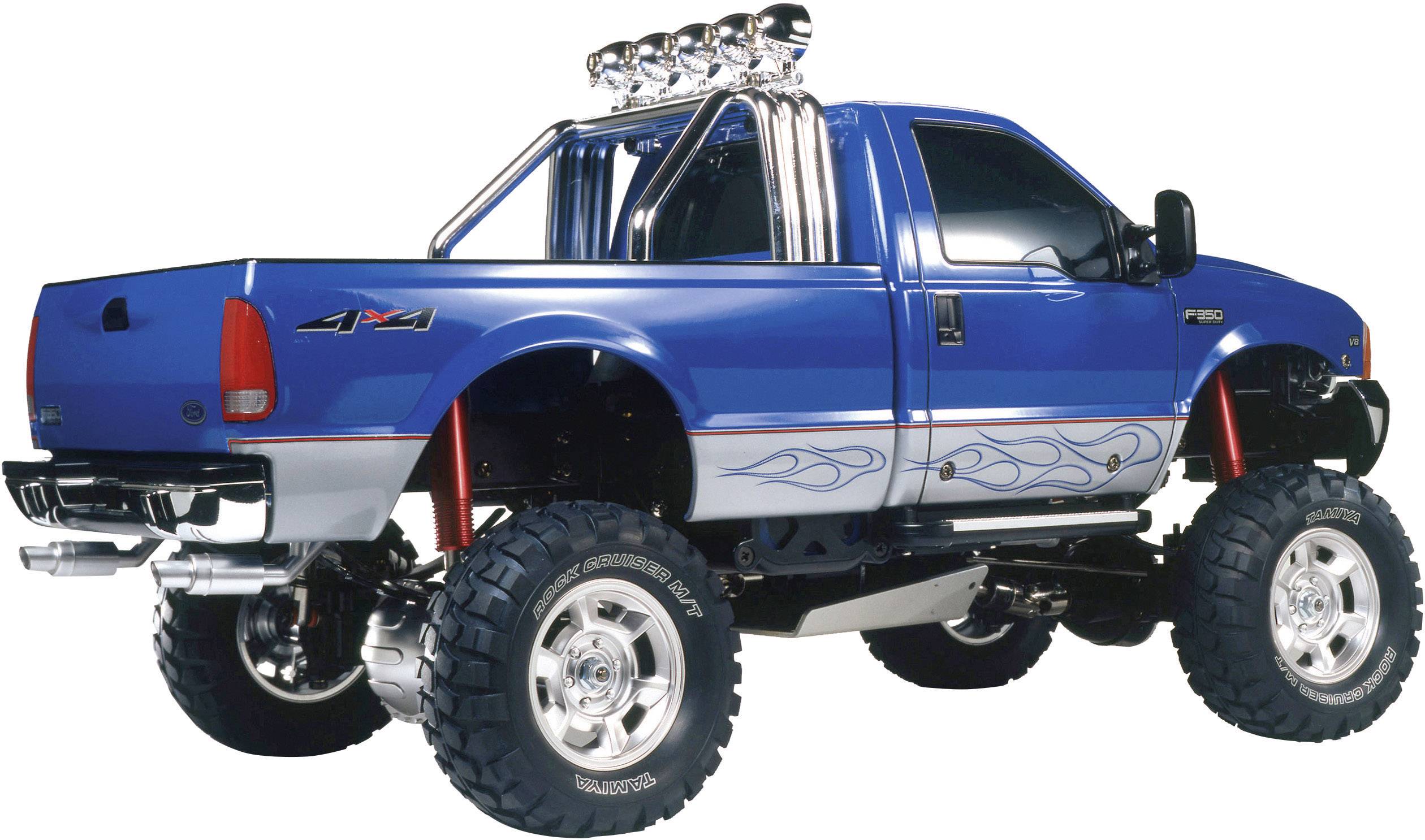 Ein blauer, erhöhter Pickup-Truck mit großen Reifen und Flammen-Designs an der Seite, geparkt auf einer weißen Fläche.