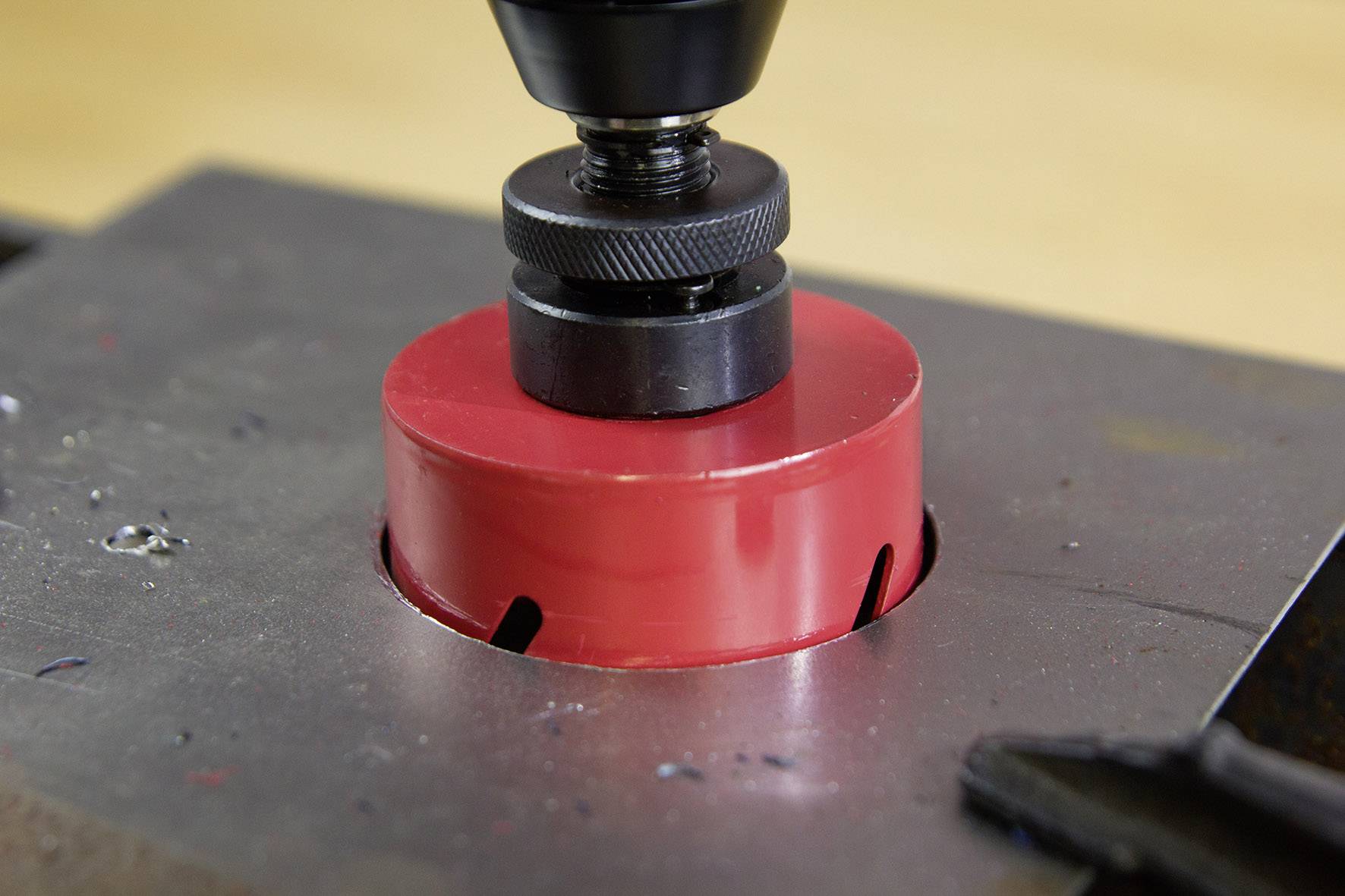 Bohrmaschine mit roter Lochsäge schneidet präzise ein rundes Loch in eine Metallplatte. Nahaufnahme zeigt den Arbeitsvorgang.