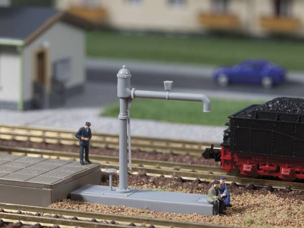 Modelleisenbahn-Szene: Eine Dampflokomotive wird auf einem Gleis von drei Figuren betrachtet. Eine Wasserpumpe steht am Gleisrand.