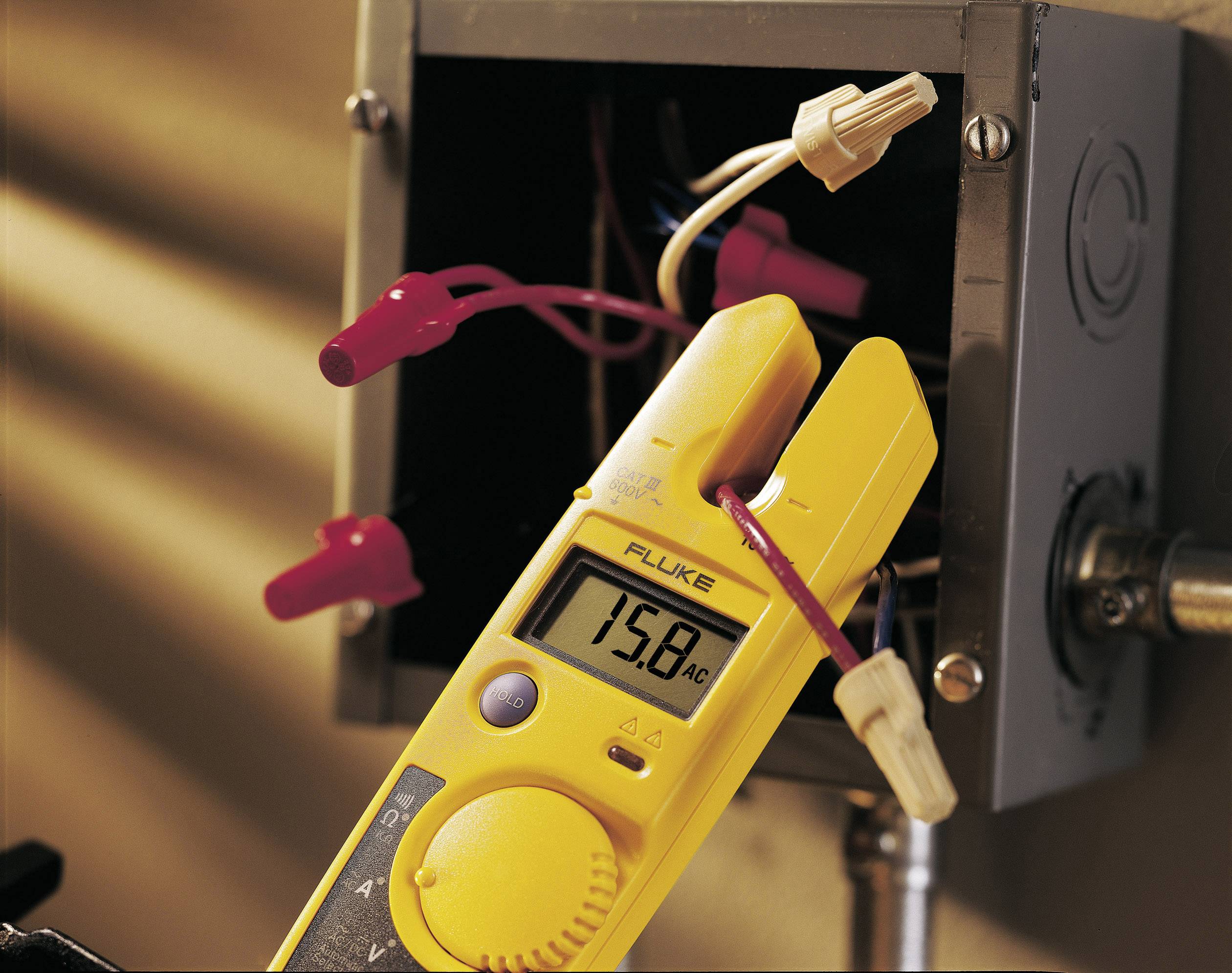 Ein gelbes Multimeter misst 15,8 Ampere Wechselstrom an einem geöffneten Anschlusskasten mit sichtbaren Drähten und Verbindern.
