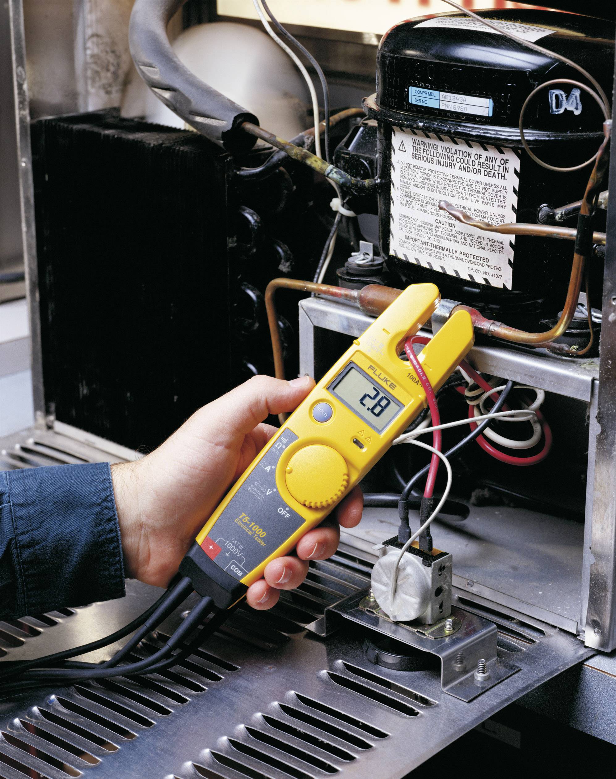 Eine Person misst mit einem digitalen Multimeter die elektrische Spannung einer Klimaanlage, die 28 Volt anzeigt.