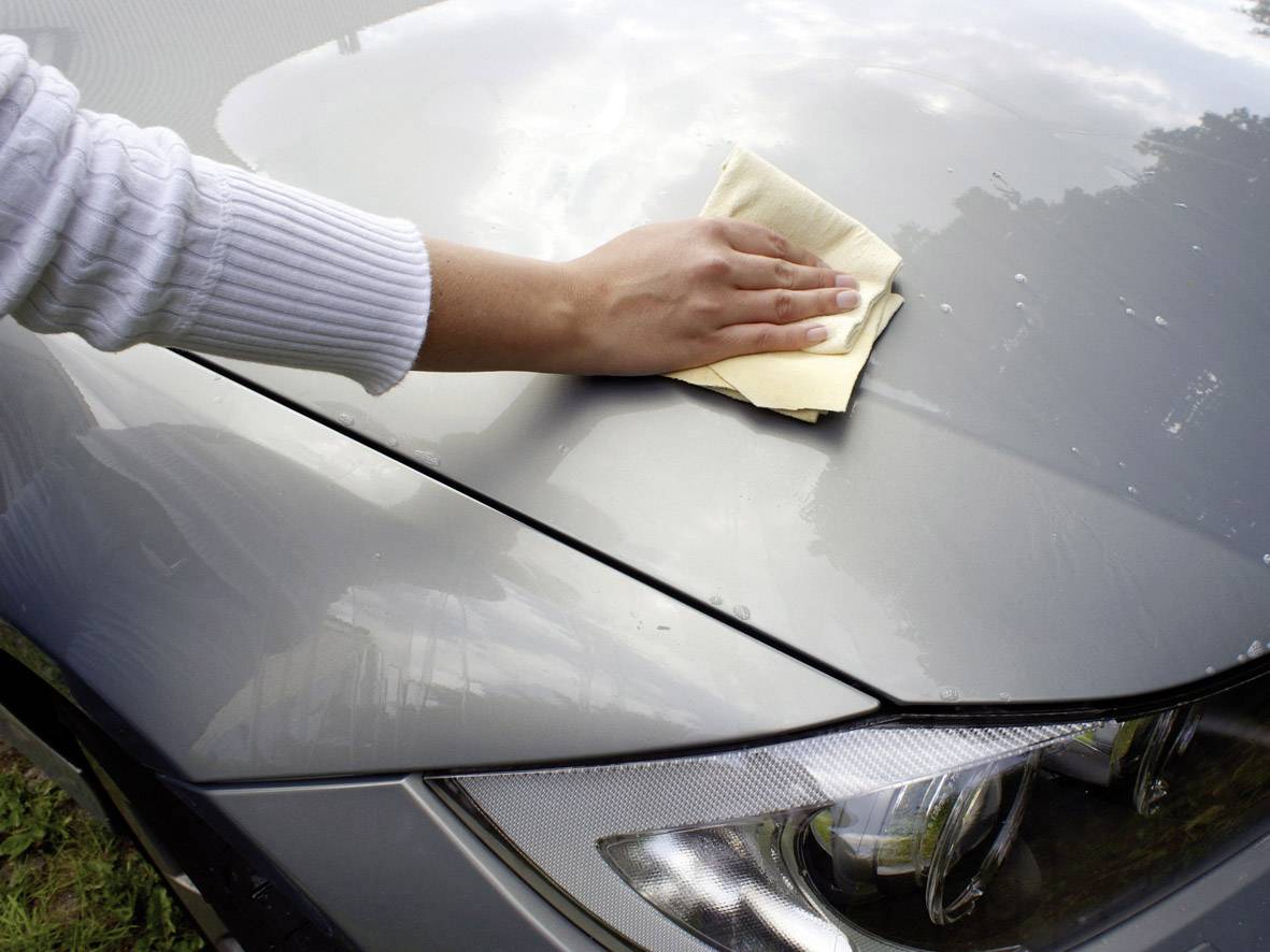 Eine Hand wischt mit einem Tuch die Motorhaube eines grauen Autos ab.