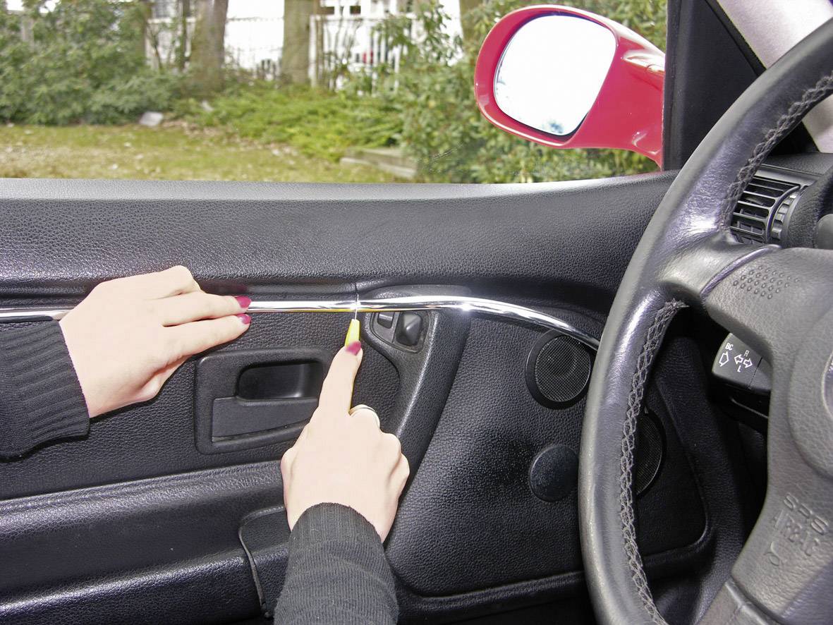 Hände benutzen ein Werkzeug, um die Innenverkleidung einer Autotür zu lösen.