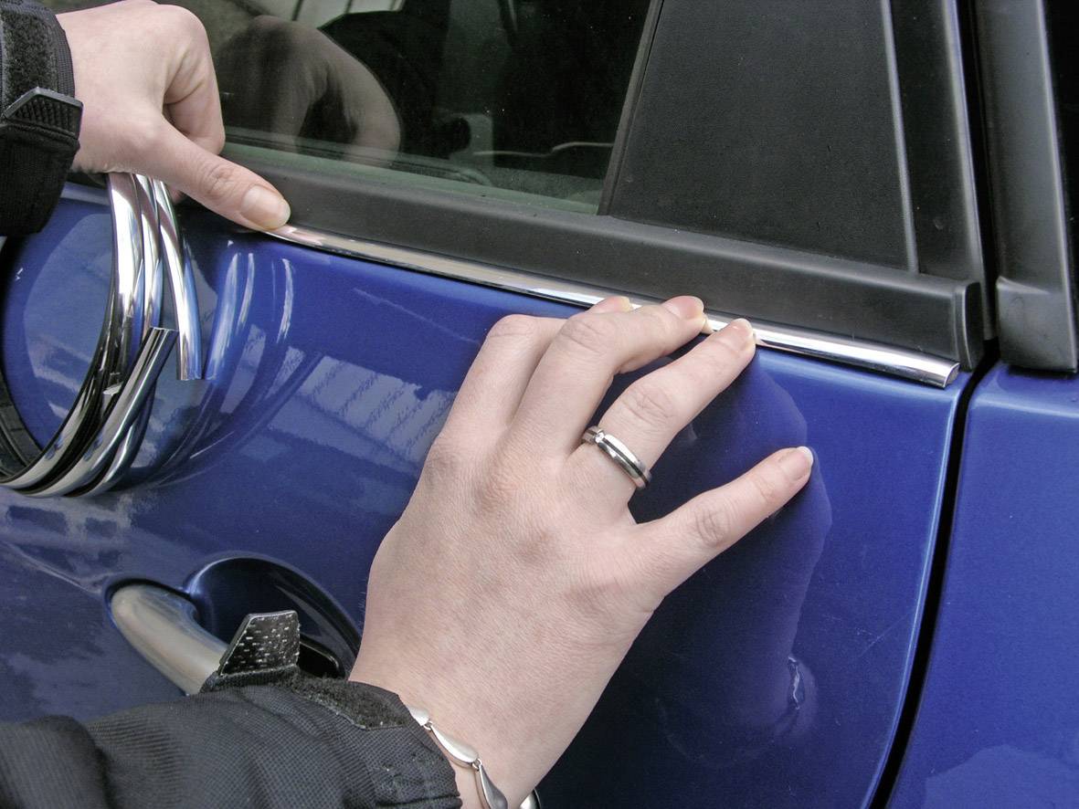 Jemand befestigt eine Zierleiste an der Autotür eines blauen Fahrzeugs. Hände drücken die Leiste fest und richten sie aus.