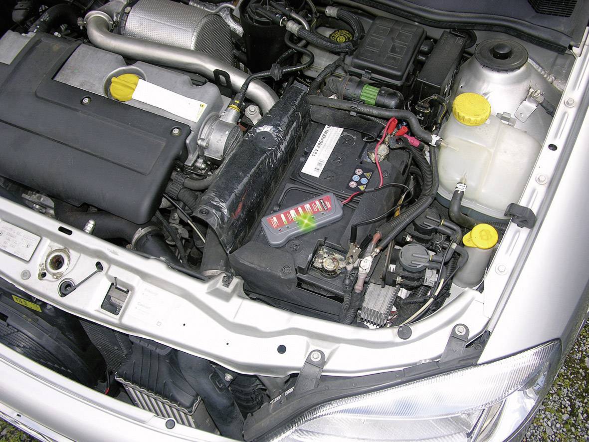 Motorraum eines Autos mit sichtbarer Batterie, Kühler und Motor. Verschiedene Teile sind durch gelbe Verschlüsse gekennzeichnet.