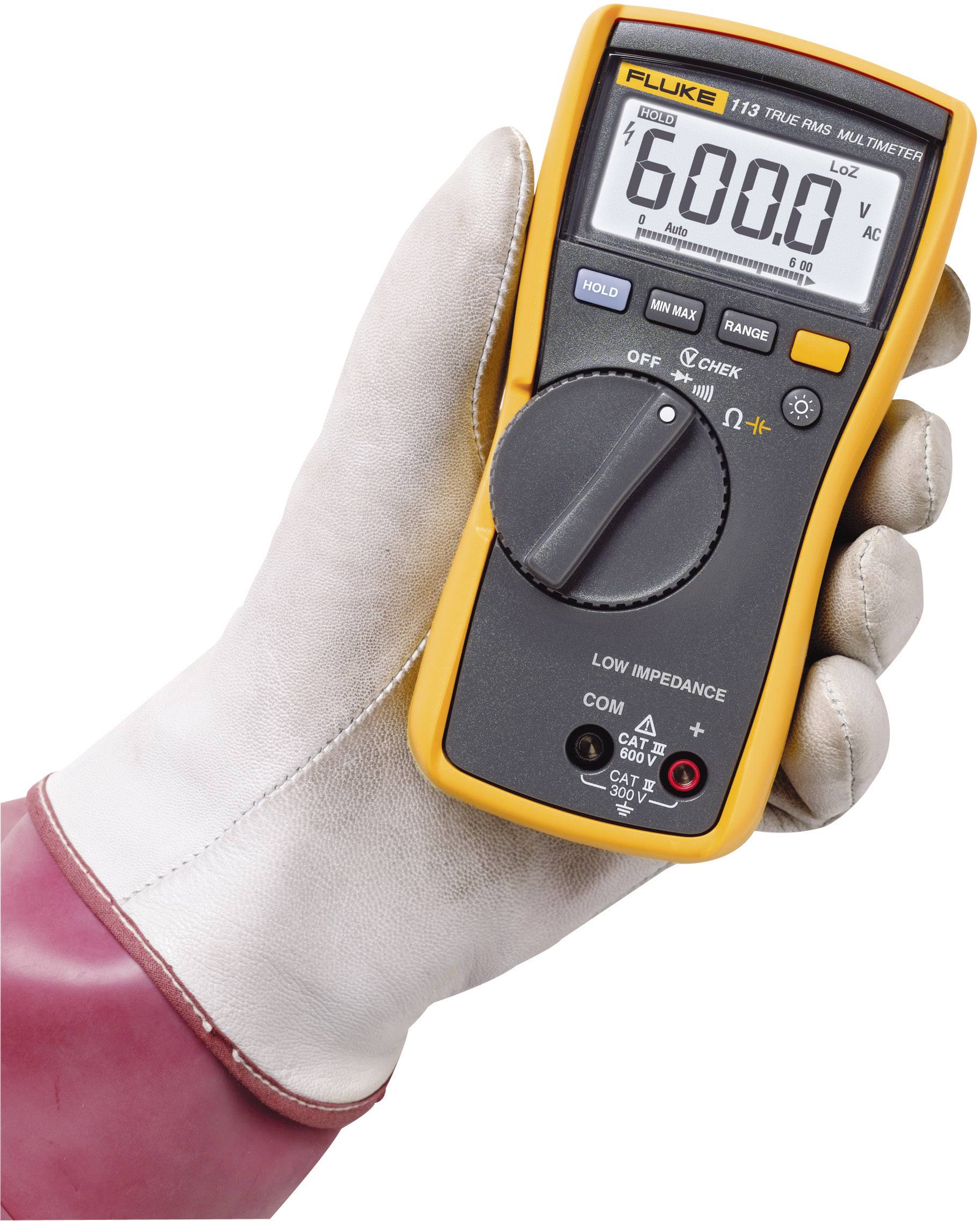 Hand hält ein gelbes Multimeter mit schwarzer Front. Display zeigt '600.0'. Person trägt einen Schutzanzug und einen Handschuh.