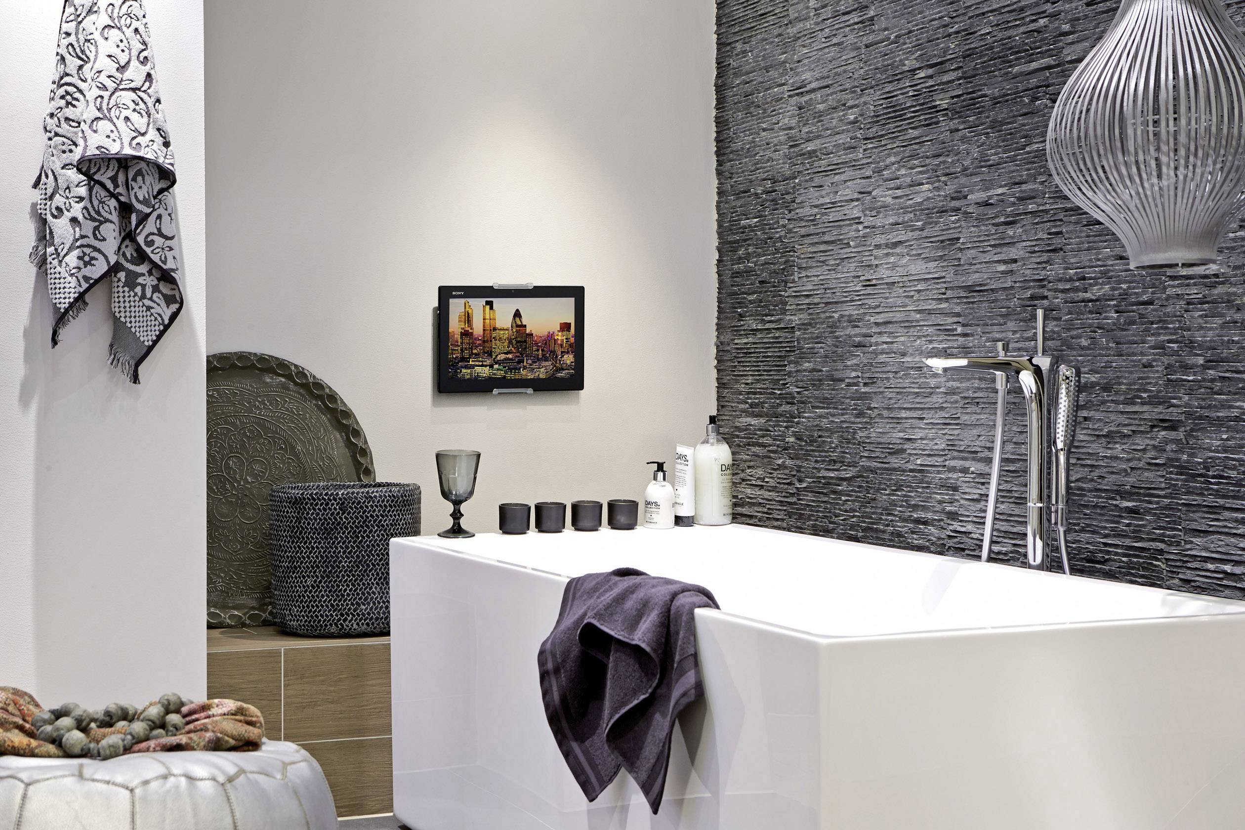 Modernes Badezimmer mit freistehender Badewanne, schwarzer Wandverkleidung, dekorativen Handtüchern und stilvoller Beleuchtung.