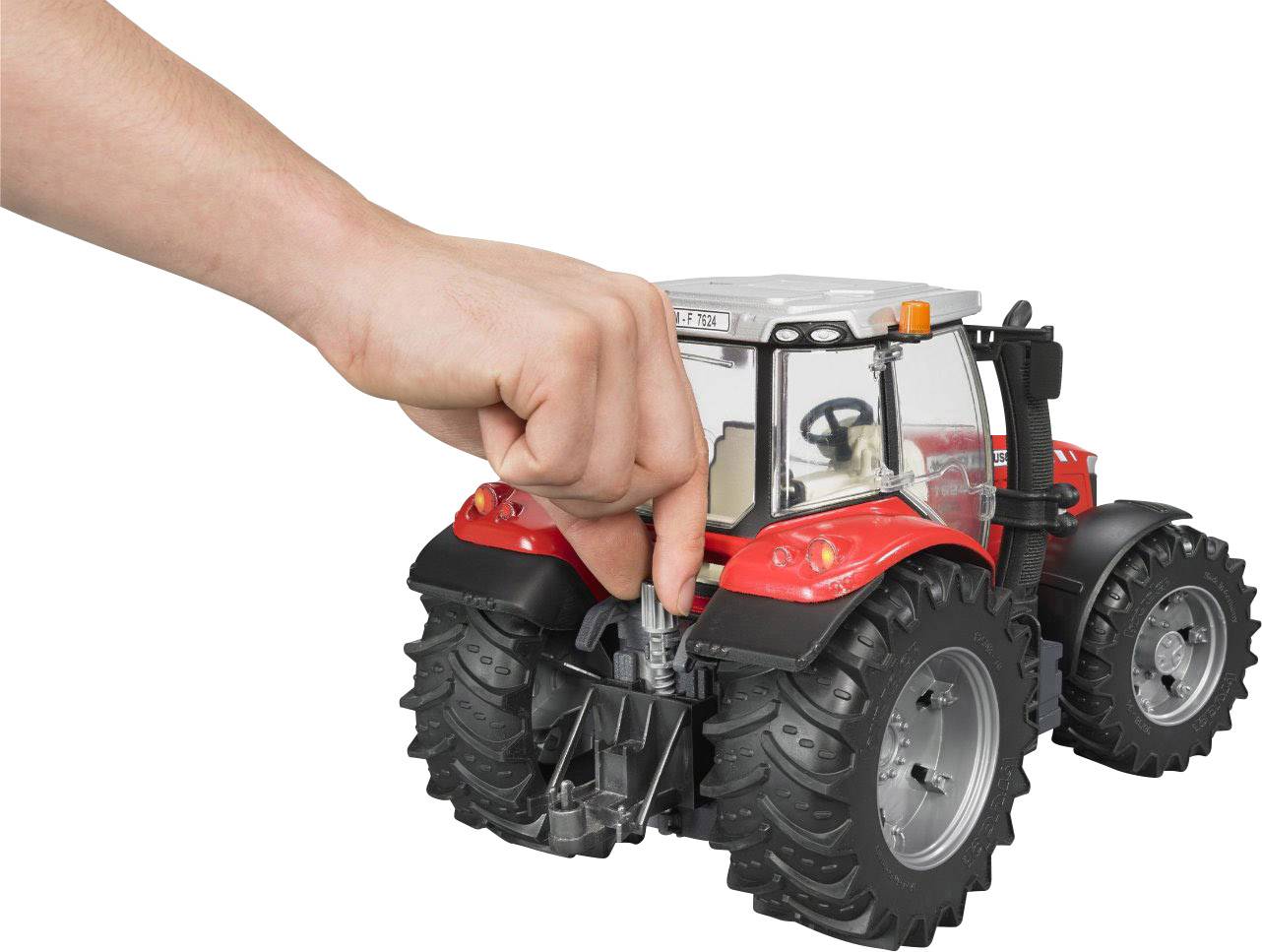 Ein Modelltraktor wird von einer Hand von oben gehalten. Der Traktor ist rot mit schwarzen Reifen und silbernen Details.